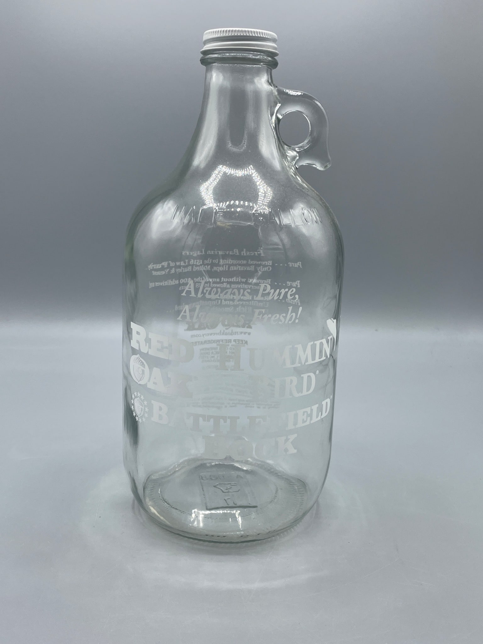 Red Oak Brewery Glass Half Gallon Growler With Handle and Screw Cap: This is a clear glass half-gallon growler produced for Red Oak Brewery, featuring etched branding that includes 'Always Pure,' 'Red Oak,' 'Battlefield Bock,' and other details about the brewery and