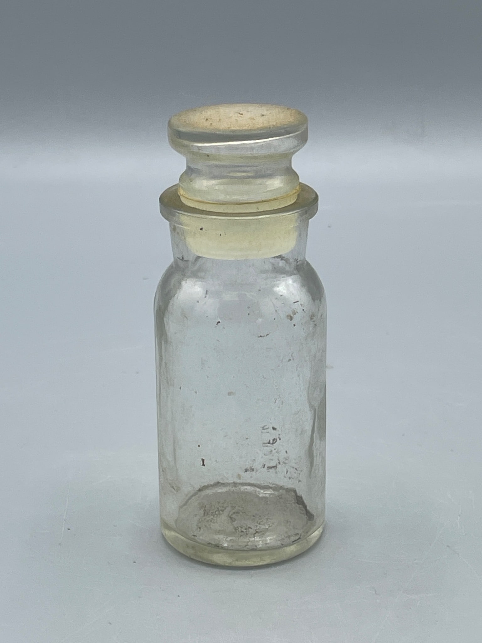 Clear Glass Stoppered Bottle with Double-Ended Cap, Approx. 4.5 Inches Tall: This is a clear glass bottle with a detachable stopper. It features cylindrical construction and measures approximately 4.5 inches in height, as seen next to a ruler. The bottle is shown with its