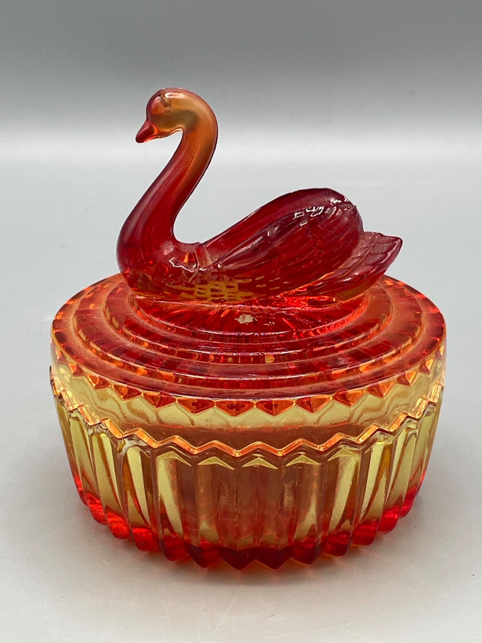 Pressed Glass Swan-Shaped Lidded Dish in Amberina Colorway: This lot features a lidded pressed glass dish with a swan-shaped top, designed in an amberina colorway, transitioning from red to yellow. The piece measures approximately 5 inches in height, and the