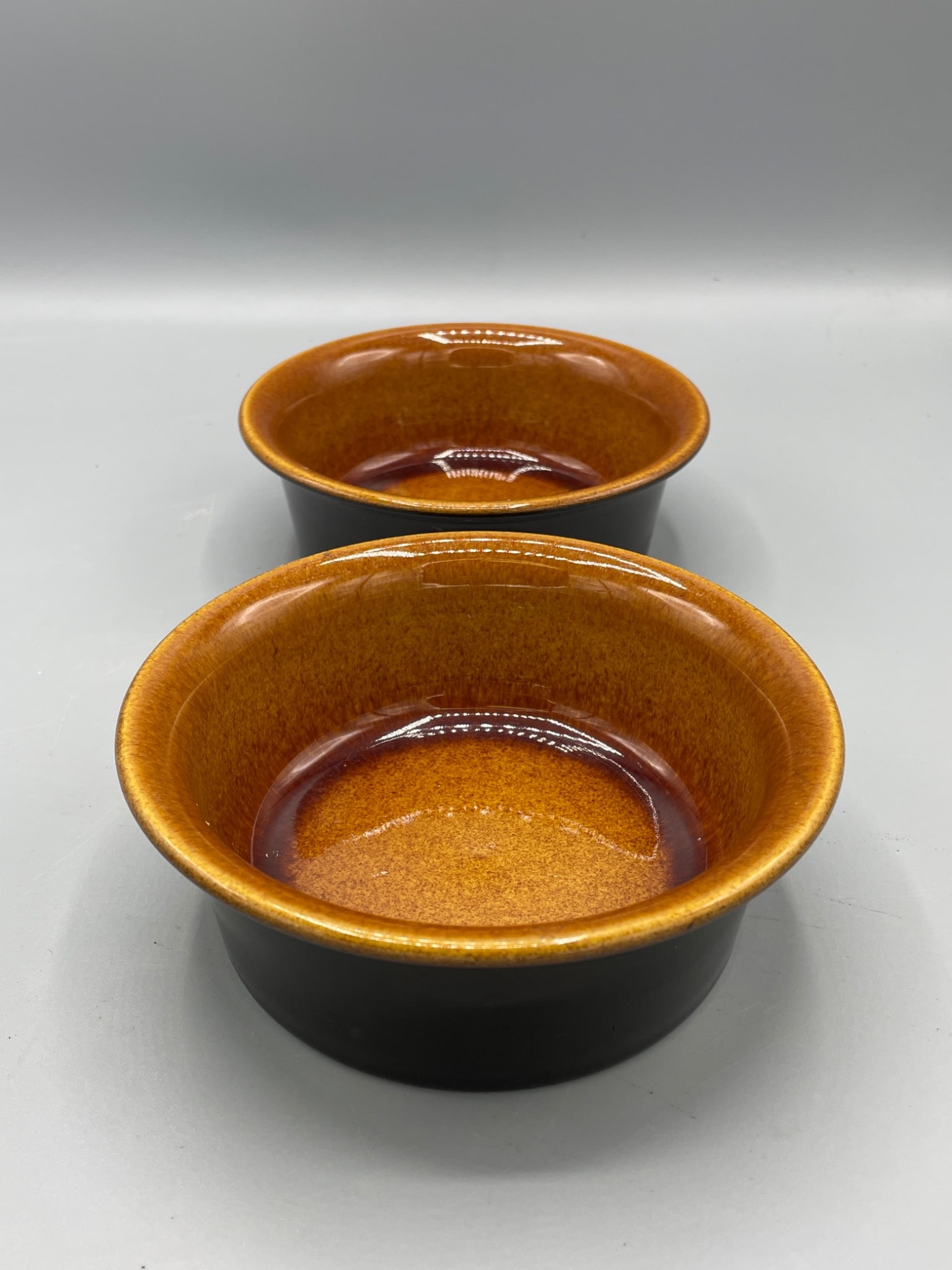 Two Octagon USA Ceramic Bowls With Amber Glaze: This set includes two ceramic bowls marked 'Octagon USA' on the underside. The bowls feature an amber glaze interior and a black glaze exterior. Both are approximately 2.5 inches in height and have a 