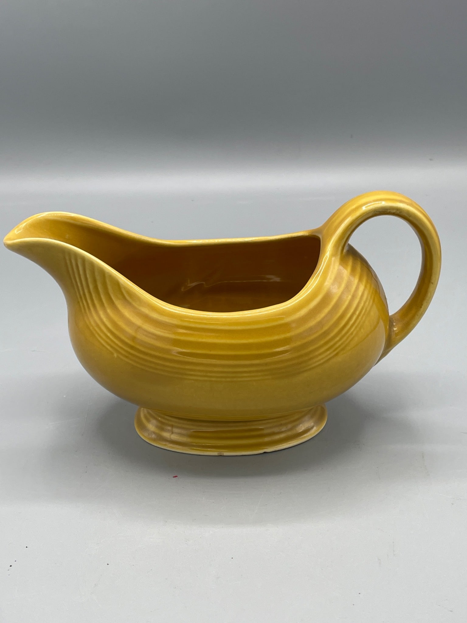 Yellow Ceramic Gravy Boat with Handle and Footed Base, Unknown Maker: This is a yellow ceramic gravy boat featuring a single handle and a footed base. It has smooth, curved lines and a ribbed design near the top. The dimensions, as noted with a ruler in the image, sugge
