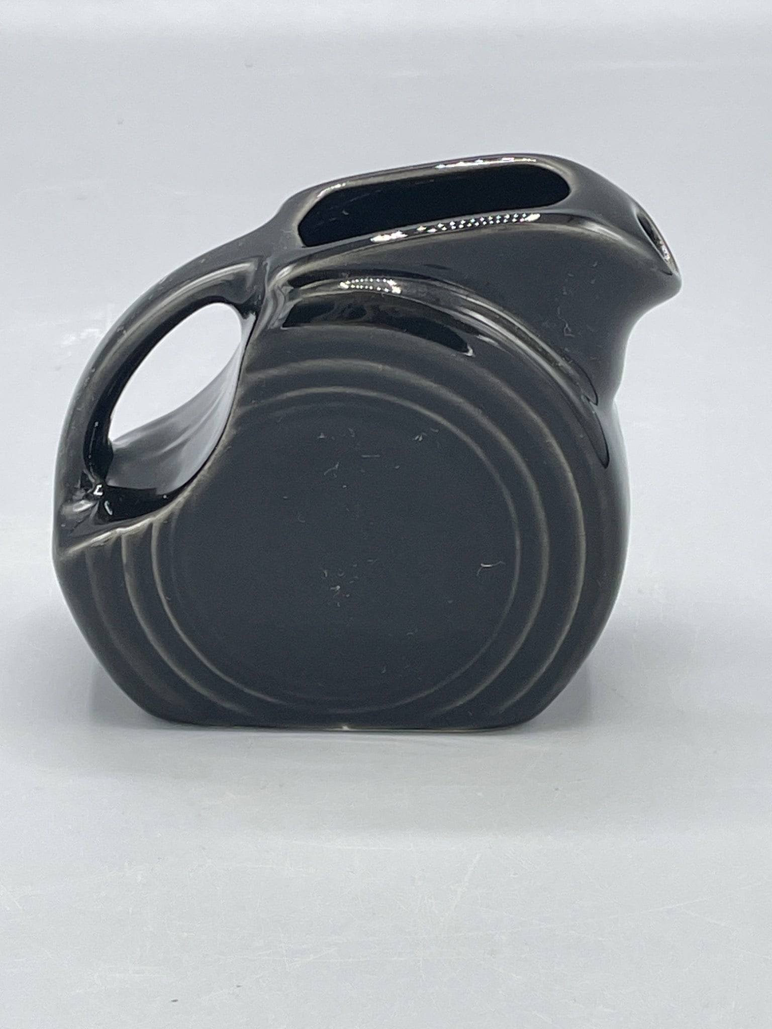 Fiesta Black Ceramic Pitcher With Embossed Mark on Base: This is a black ceramic pitcher featuring a circular design motif. The item has an embossed mark on the base, providing an identifier. Its dimensions are visible next to a ruler for reference. The