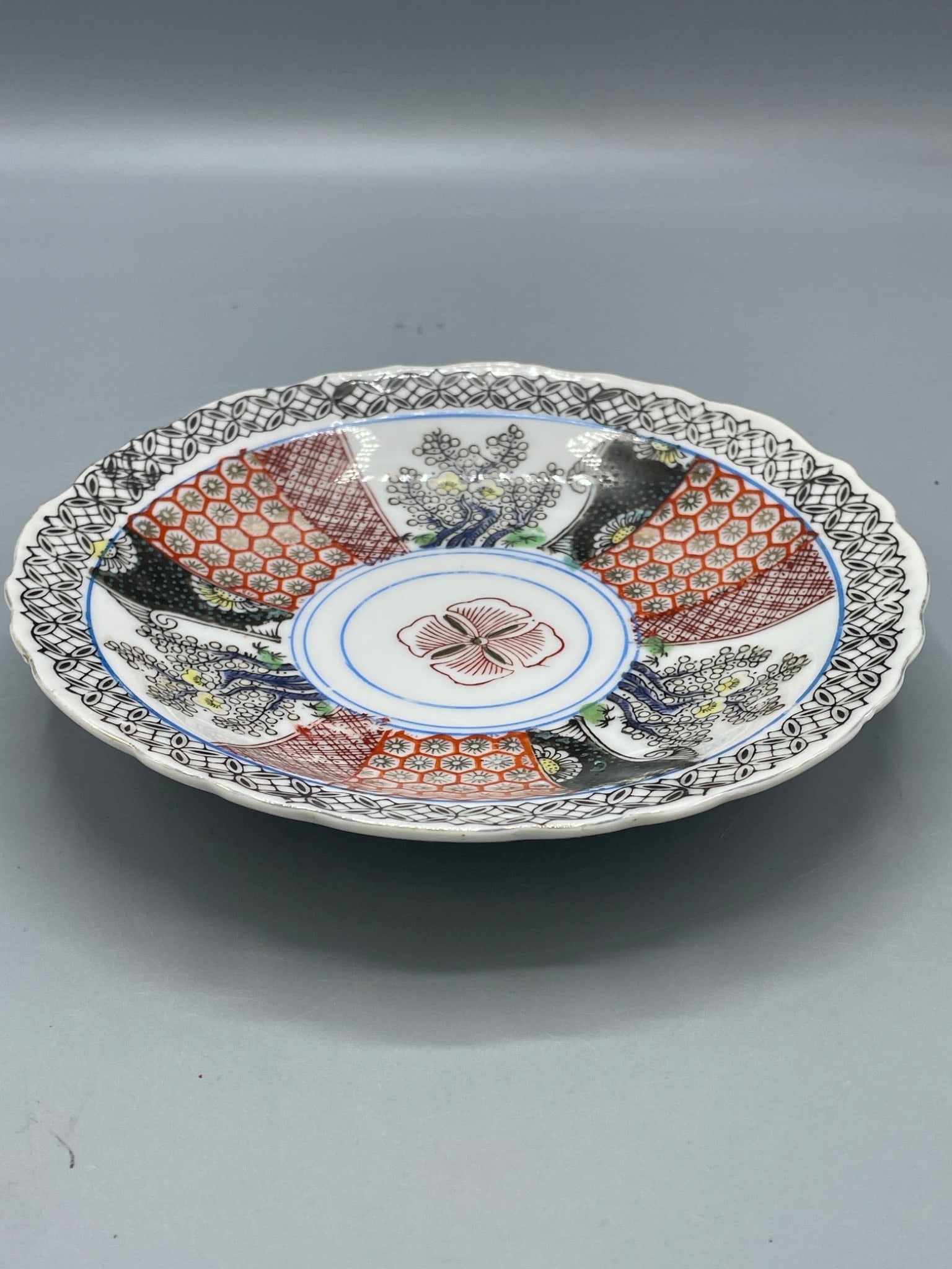 Goldcastle Hand-Painted Plate Made in Japan with Intricate Pattern: This is a hand-painted plate marked 'Goldcastle Made in Japan' on the underside. The plate features a scalloped edge, intricate designs in a multi-color pattern with red, blue, black, and gold