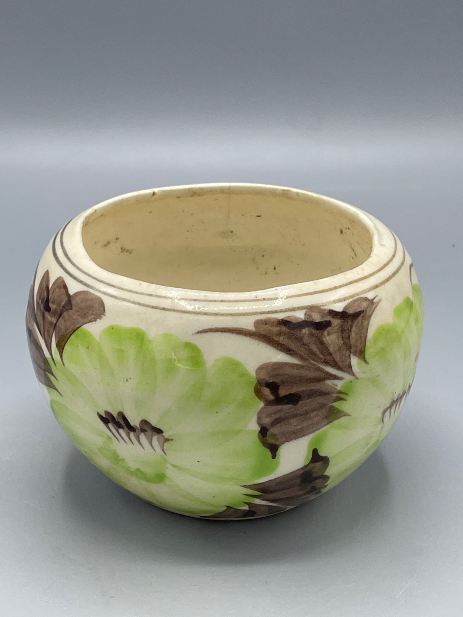 Decorative Ceramic Flower Pot With Handpainted Design: This ceramic flower pot features a handpainted floral design with green and brown hues. It measures approximately 3 inches in height, as shown, and has a drainage hole at the bottom. 'MEX' is marked b