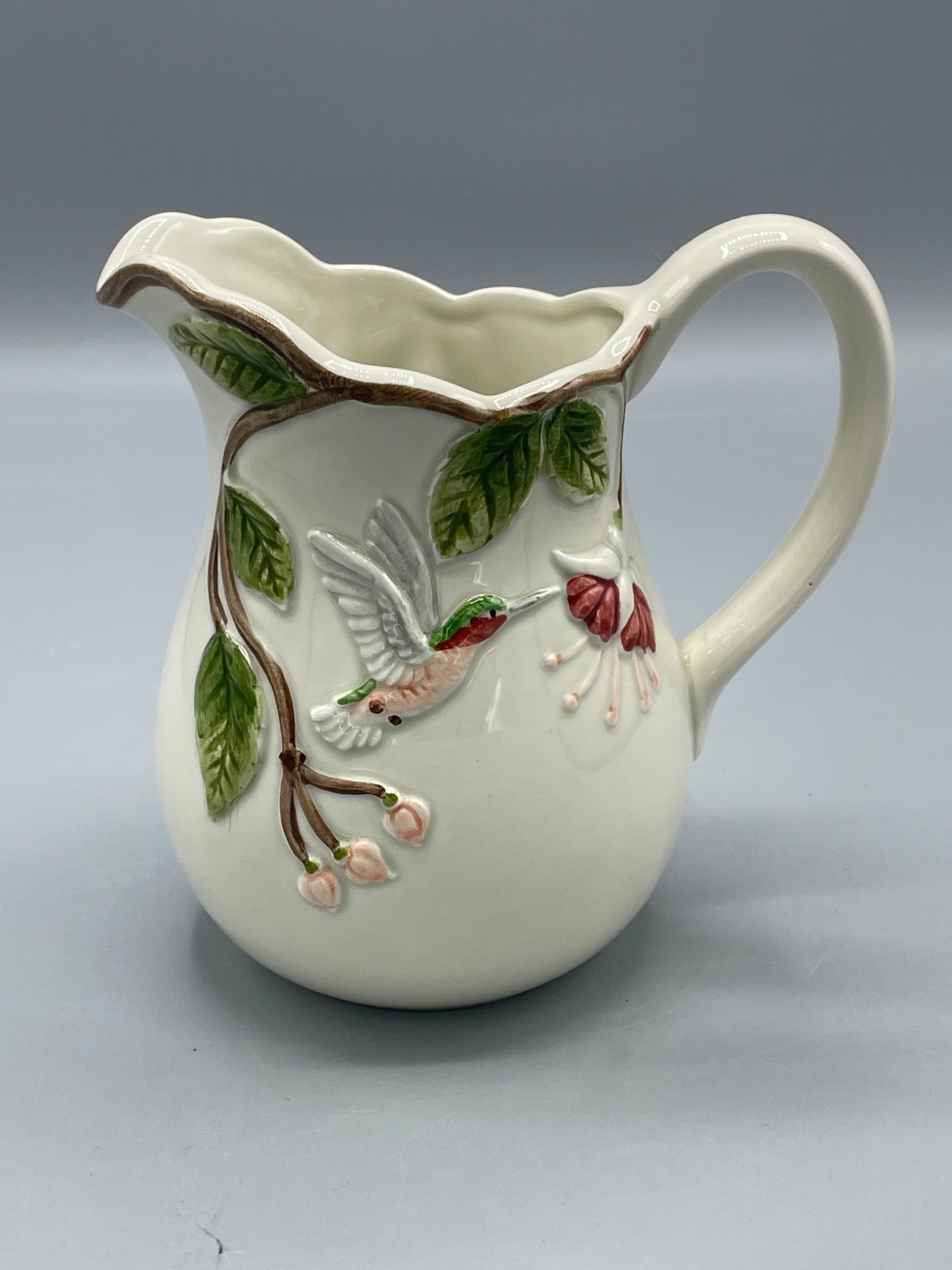 Otagiri Handcrafted Ceramic Pitcher with Hummingbird and Floral Design: A handcrafted ceramic pitcher made by Otagiri, Japan, featuring an embossed hummingbird and floral design. The bottom is stamped with Â© OTAGIRI and retains the original 'Handcrafted' sticke