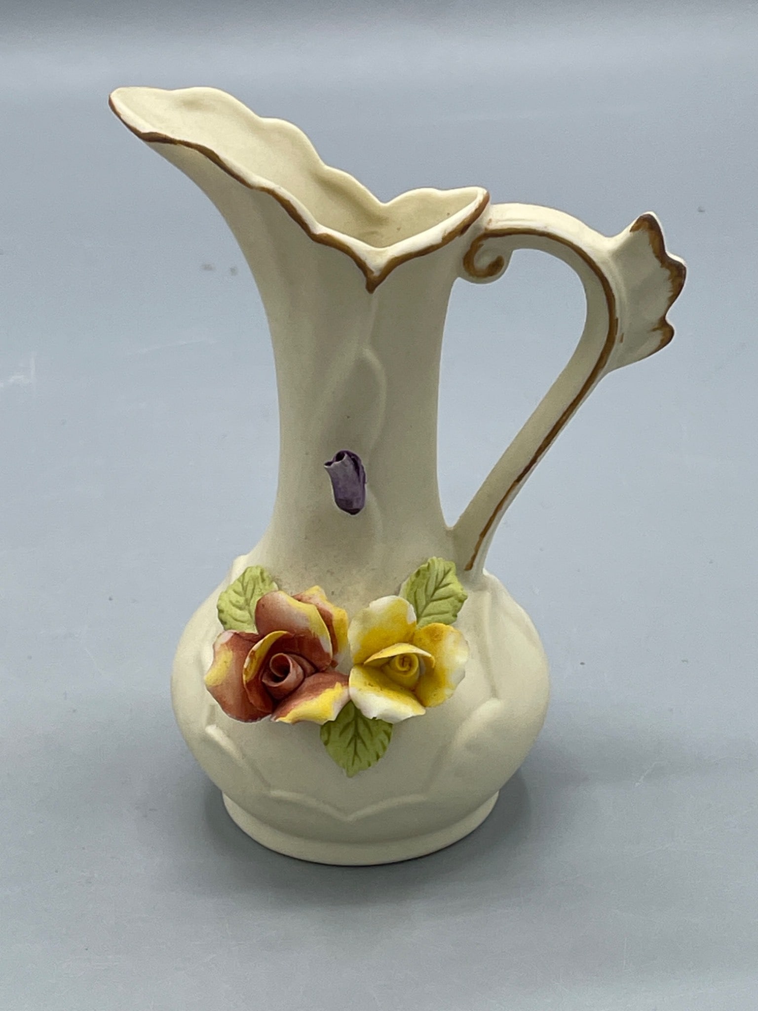 Hand-Painted Ceramic Pitcher with Floral Embellishments, Approx. 6 Inches: This ceramic pitcher features hand-painted floral embellishments in multiple colors, with a ruffled rim accented by gold trim. It bears a floral hallmark and inscriptions on the underside, partially