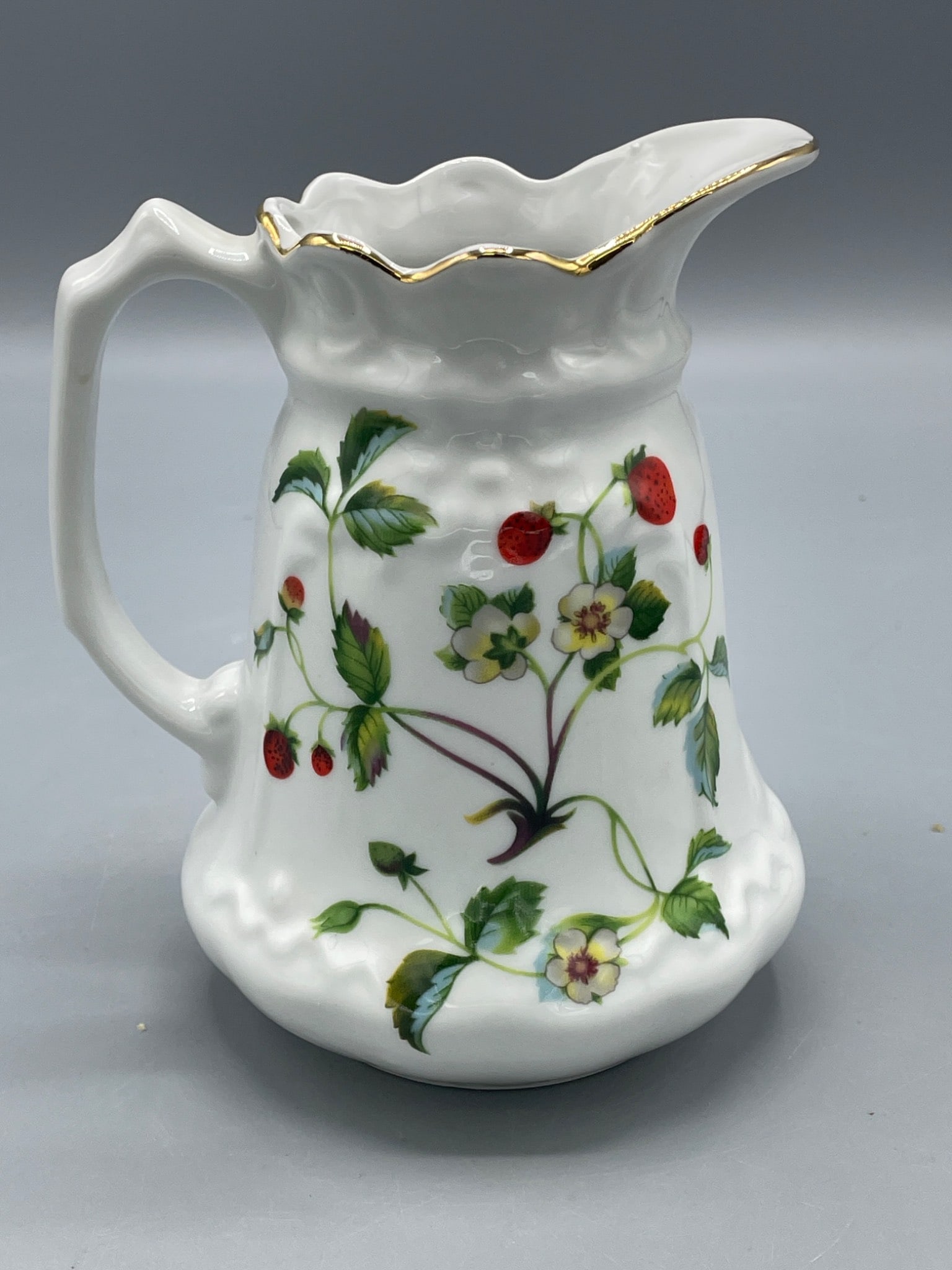 London Pottery Ceramic Pitcher with Gold Trim and Strawberry Motif: This ceramic pitcher by London Pottery features a floral and strawberry motif and a gold trim. The pitcher has a height of approximately 6 inches, as shown in the image with a scale. It has a scallope