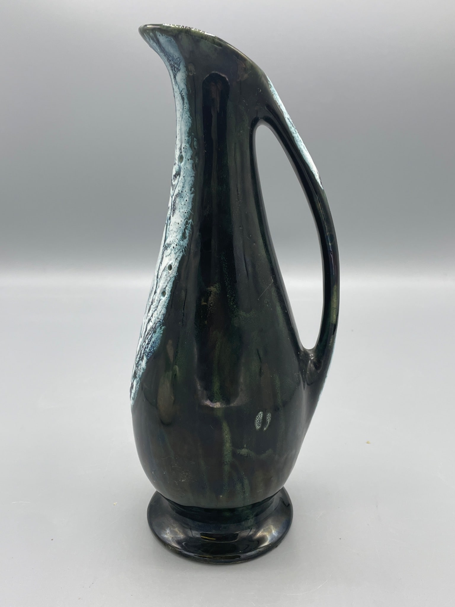Ceramic Pitcher with Handle and Glaze Finish, Marked on Base: This ceramic pitcher stands approximately 10 inches tall and features a unique glaze finish. The piece has an integrated handle design for functional use or display purposes. The underside is marked