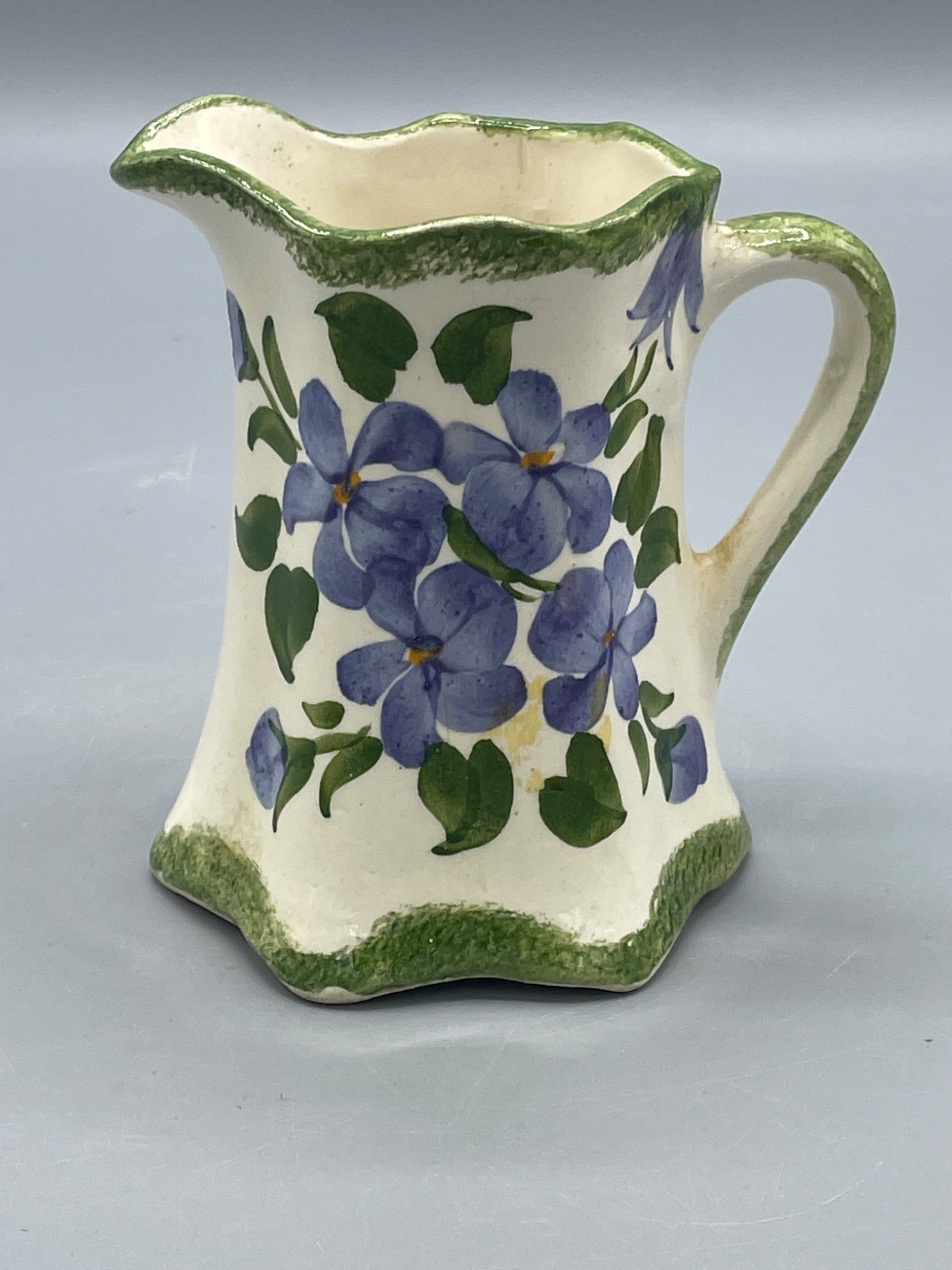 Cash Family Hand-Painted Ceramic Pitcher, USA, Floral Design: Hand-painted ceramic pitcher featuring purple flowers and green accents, created by the Cash Family in the USA. The bottom is signed 'Made by the Cash Family, Hand Painted, U.S.A.' Approximate height 
