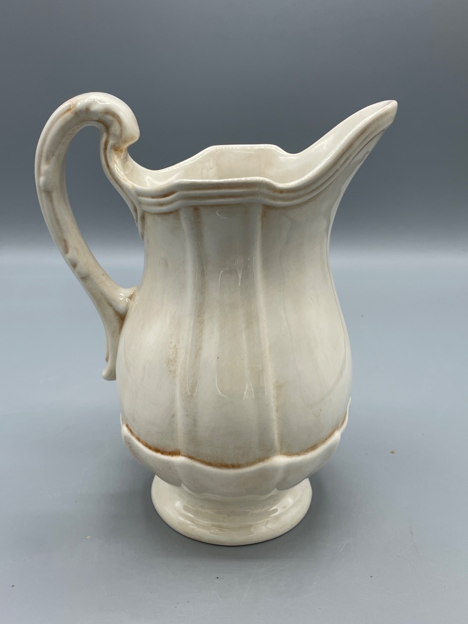 Ceramic Pitcher with Hand-Painted Finish, Made in Italy: A ceramic pitcher with a white glaze finish, marked 'Hand Painted' and 'Made in Italy' on the bottom. The pitcher stands approximately 8.5 inches tall, with decorative ribbed details and an ornately