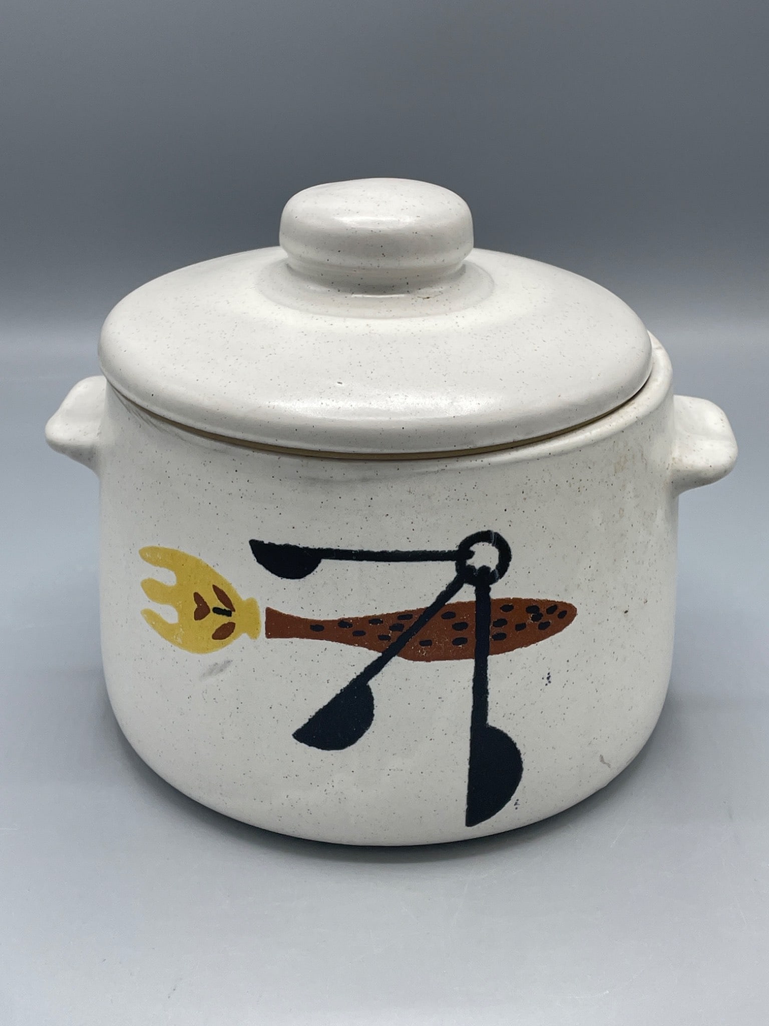 West End Ceramic Lidded Pot With Handles and Hand-Painted Design: This is a ceramic lidded pot marked 'West End' on the base. It features a hand-painted kitchen utensil design on one side. The piece includes a handled base and a matching lid. It measures