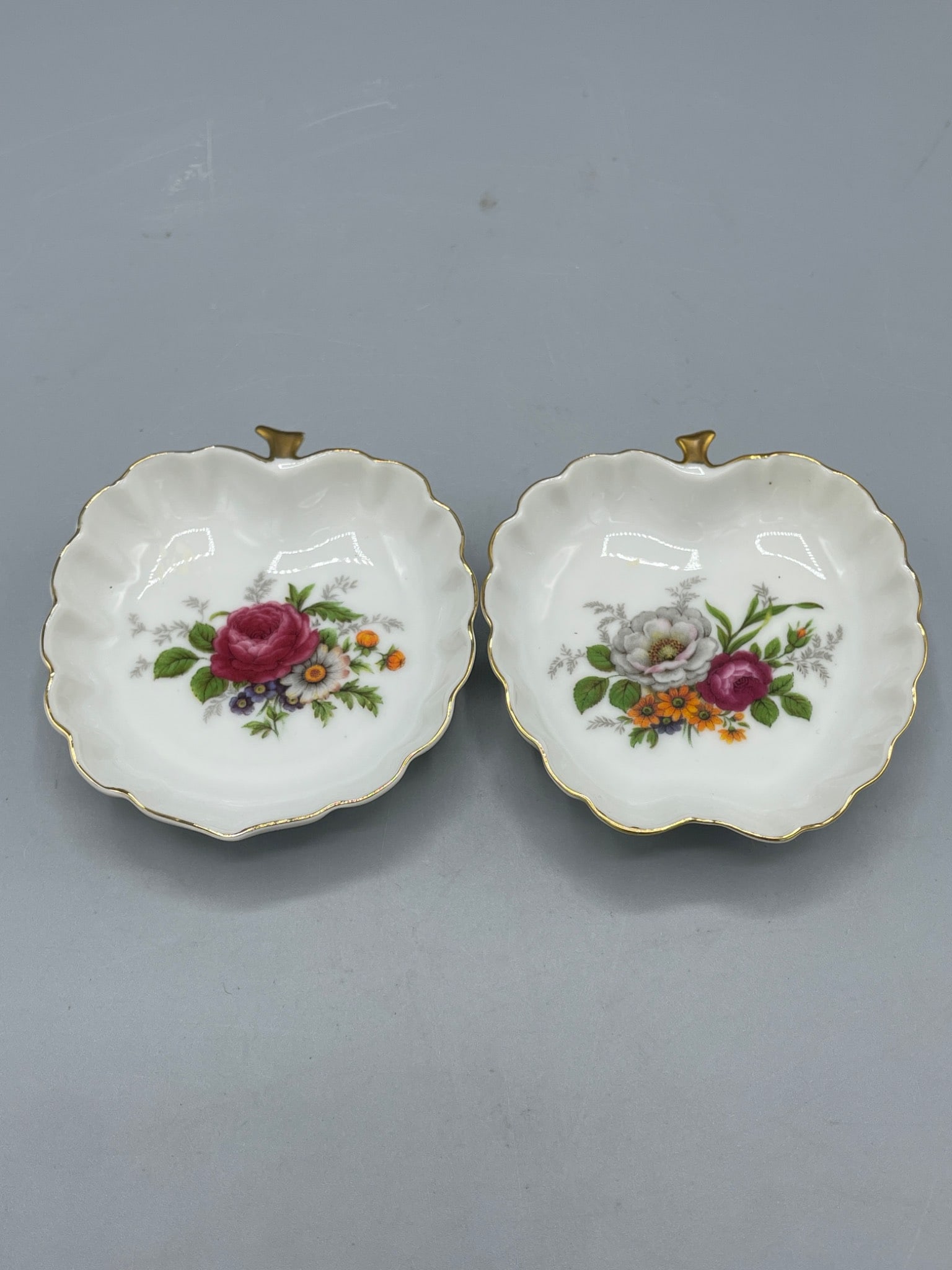 Two Decorative Floral Porcelain Dishes, Made in Japan: This lot features a set of two porcelain dishes with scalloped edges, vibrant floral patterns, and gold gilded trims. The dishes measure approximately 3.5 inches in width and have an apple-shaped