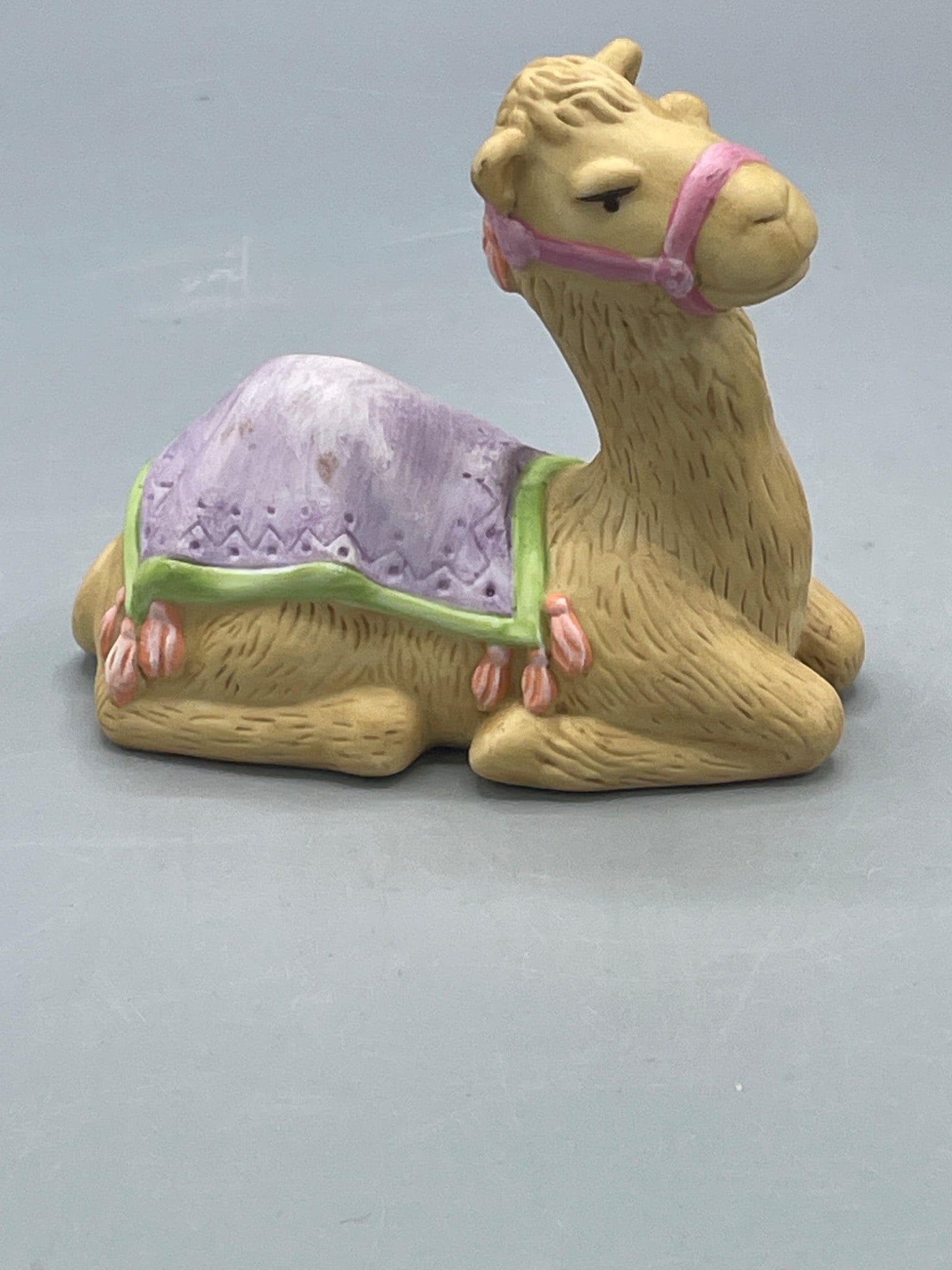 Avon 1986 Heavenly Blessings Nativity Collection Camel Figurine: This is an Avon camel figurine from the 1986 Heavenly Blessings Nativity Collection. It features a painted design with a purple blanket and pink accents. The underside is stamped 'Source of Fine