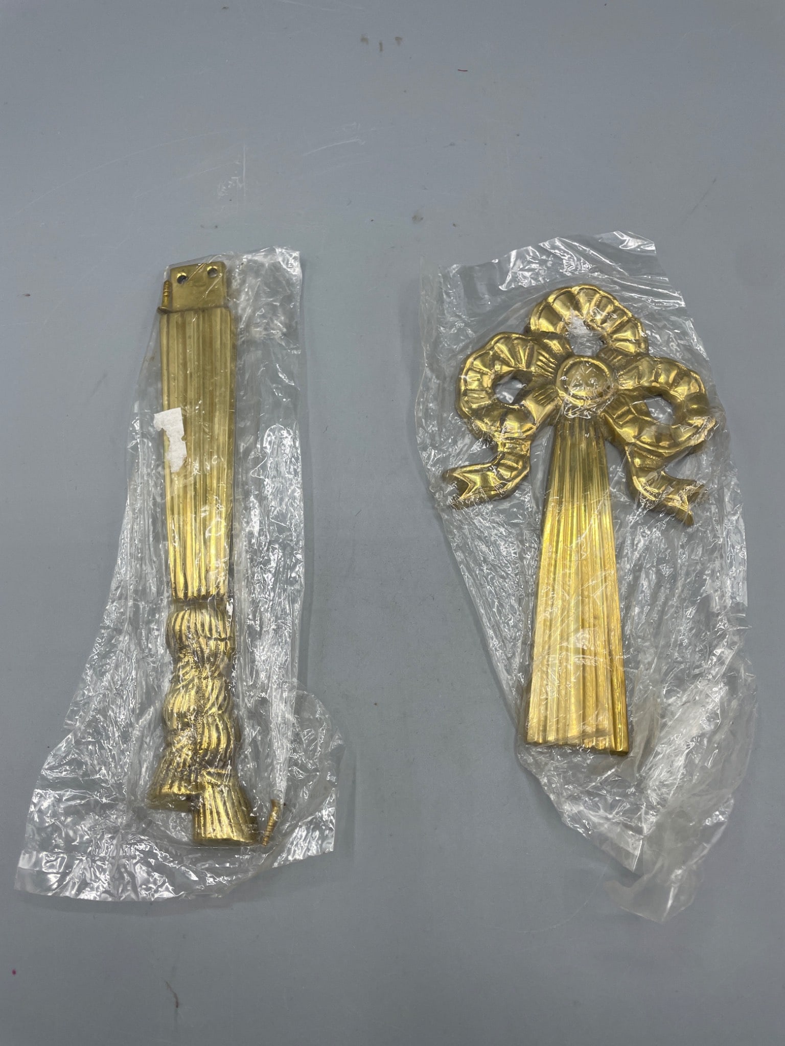 Gold-Tone Decorative Wall Plaque Components, Bow and Ribbon Motif: Two decorative wall plaque components featuring a gold-tone finish with bow and ribbon motifs. Items are still in plastic wrapping. Approximate measurements visible via included ruler indicate
