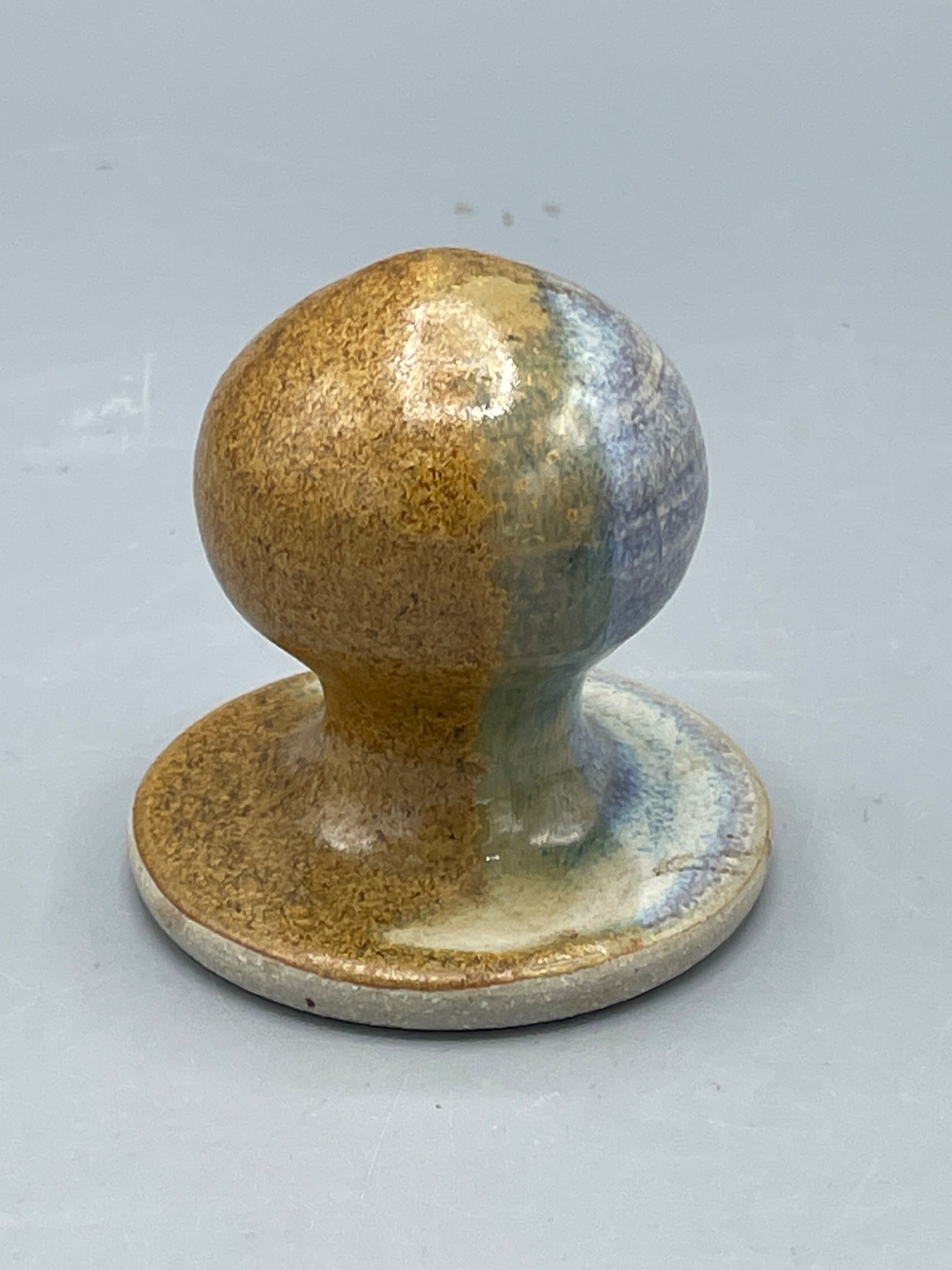 Glazed Ceramic Handheld Tool with Rounded Base: This item is a ceramic handheld tool featuring a rounded top, wide stable base, and central hole on its underside. It is finished with a multi-tone glazed surface displaying earthy hues. The