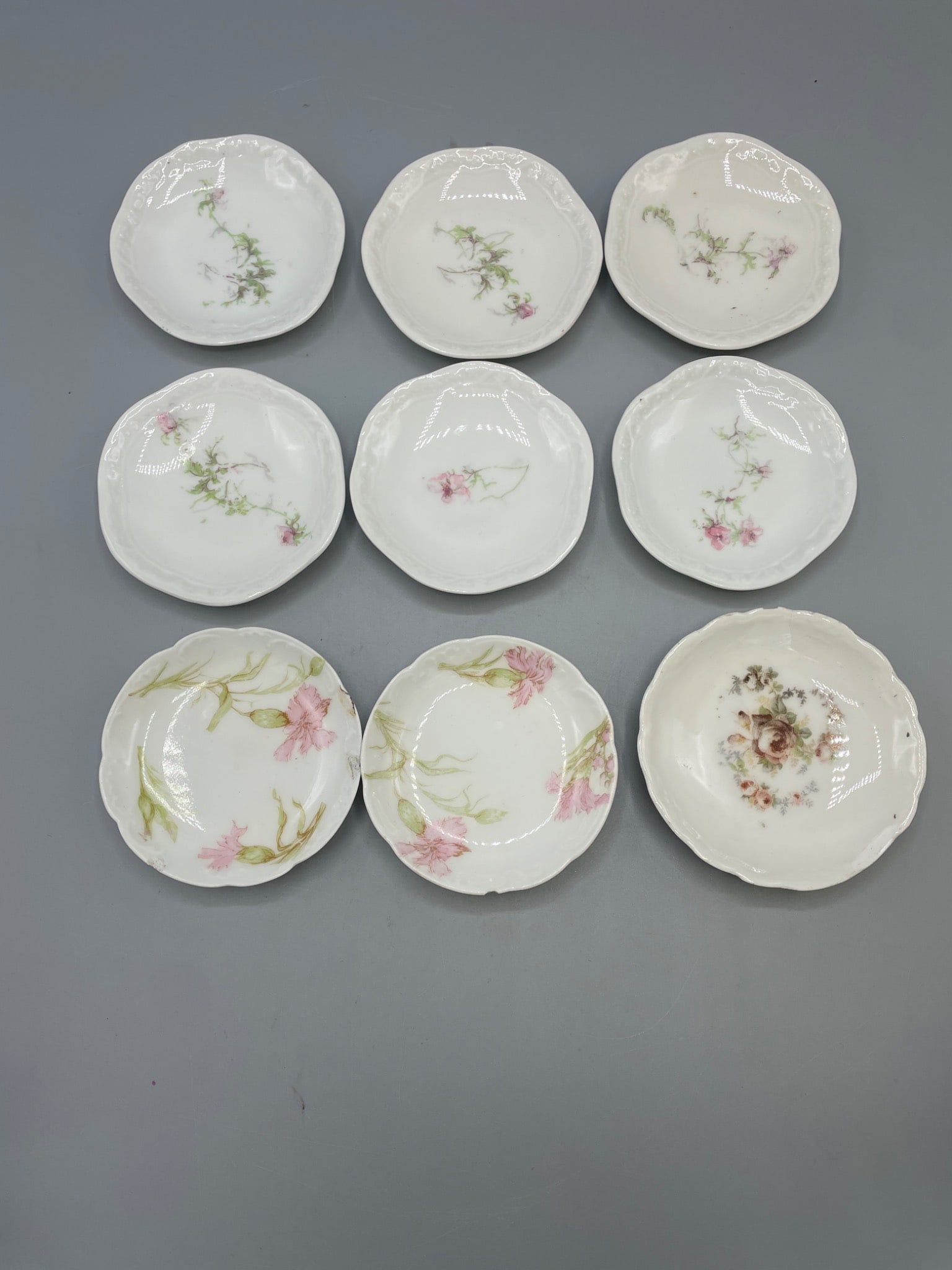 Nine Porcelain Saucers with Mixed Marks Including Limoges and KPF: This set includes nine small porcelain saucers with various floral decorations and embossed edges. Markings on the underside identify production from Limoges (Haviland & Co., A. Lanternier, and others