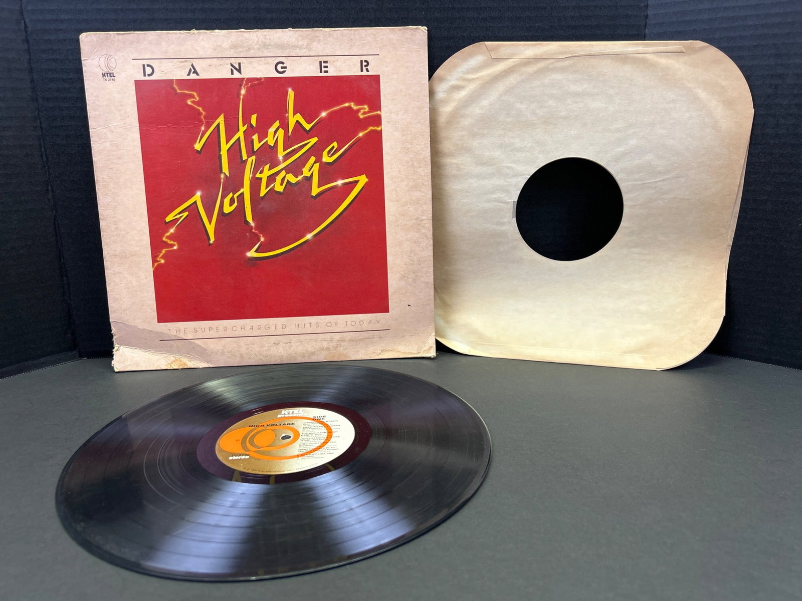 Danger - High Voltage Vinyl Record with Sleeve: This is a vinyl record album titled 'Danger - High Voltage.' The album includes its original cardboard sleeve and inner protective sleeve. The vinyl has visible scratches, indicating wear. The