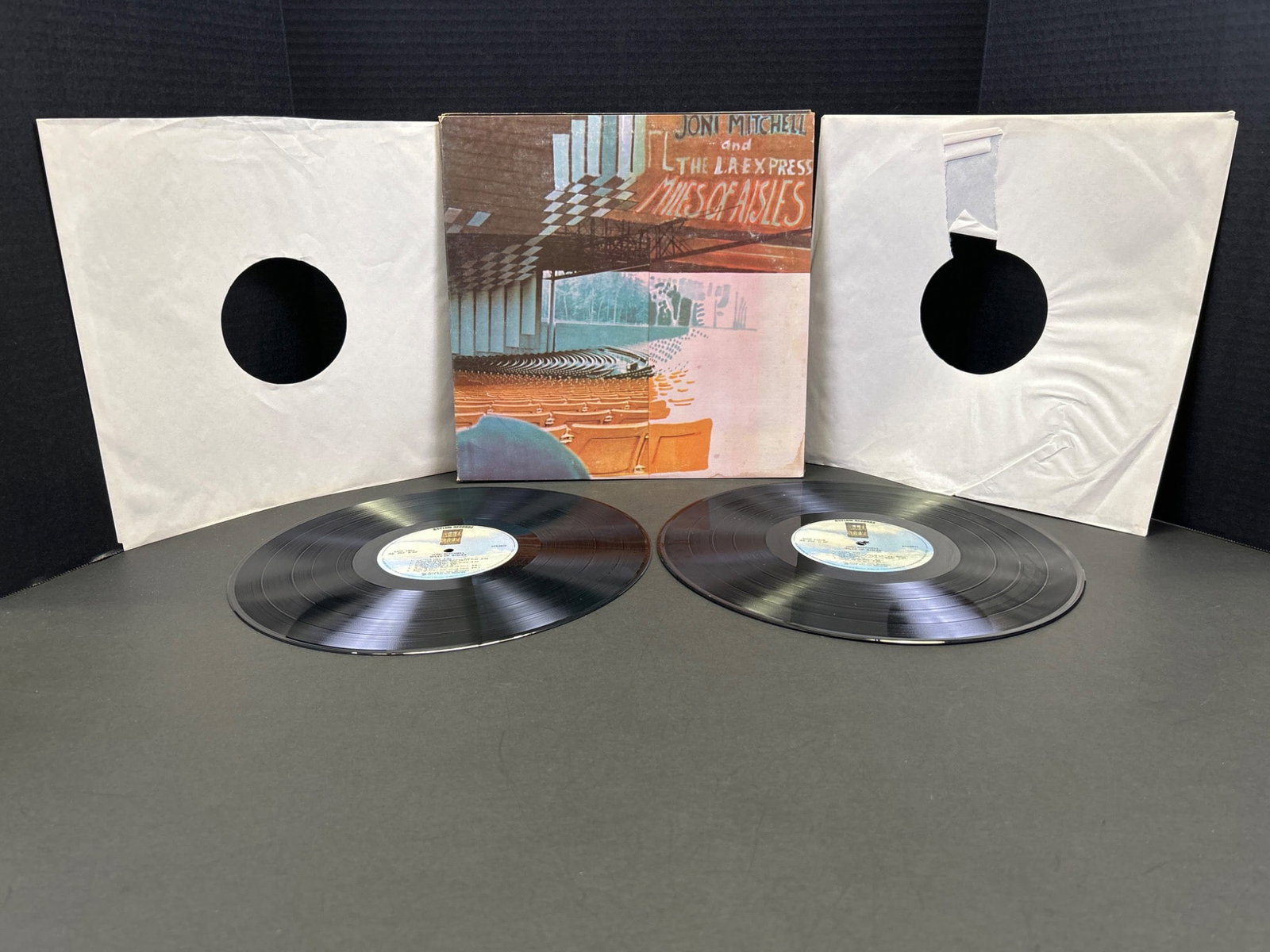 Joni Mitchell - Miles of Aisles Double Vinyl Album with Gatefold Cover: Double vinyl LP album of 'Miles of Aisles' by Joni Mitchell. Includes original gatefold cover featuring artwork and images of the artist and her band. Records show visible tracks from a 2LP set releas