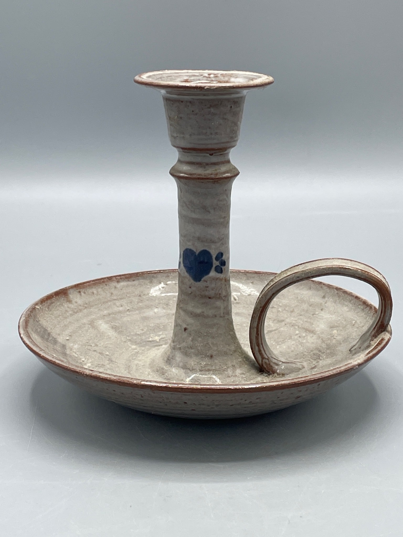 Stoneware Chamberstick Candle Holder Signed 'Owens' and Dated 1987: A handmade stoneware chamberstick-style candle holder featuring a rustic glaze with a blue heart design on the shaft. The piece includes a single ring handle and bears the signature 'Owens' and the