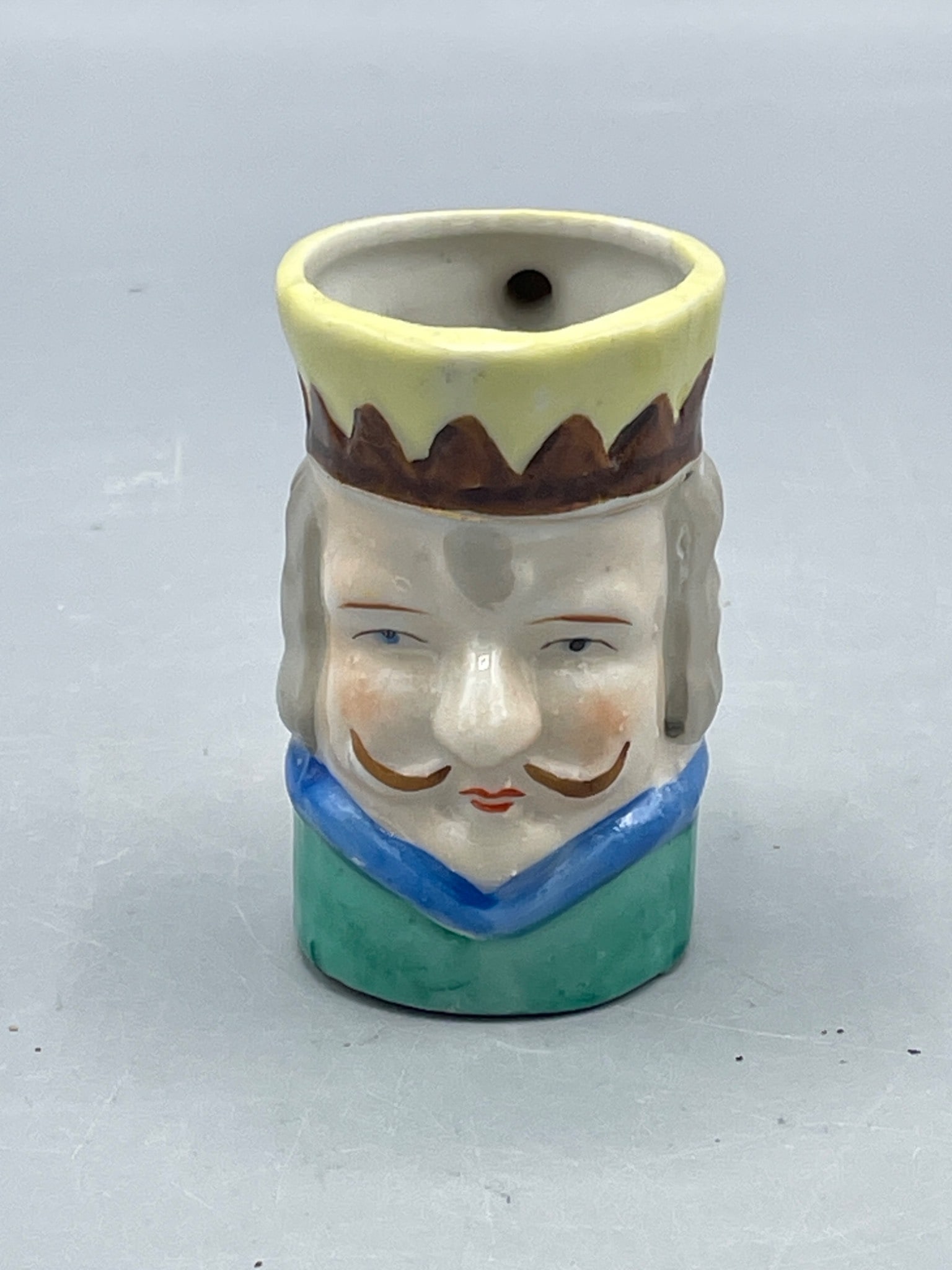 Hand-Painted Ceramic Figural Mug with 'Japan' Marking, Approx. 2.5 in. Tall: Small ceramic mug depicting a king's face, hand-painted in green, yellow, blue, and brown hues. Marked 'Japan' at the base, indicating its origin. Measuring approximately 2.5 inches in height, it