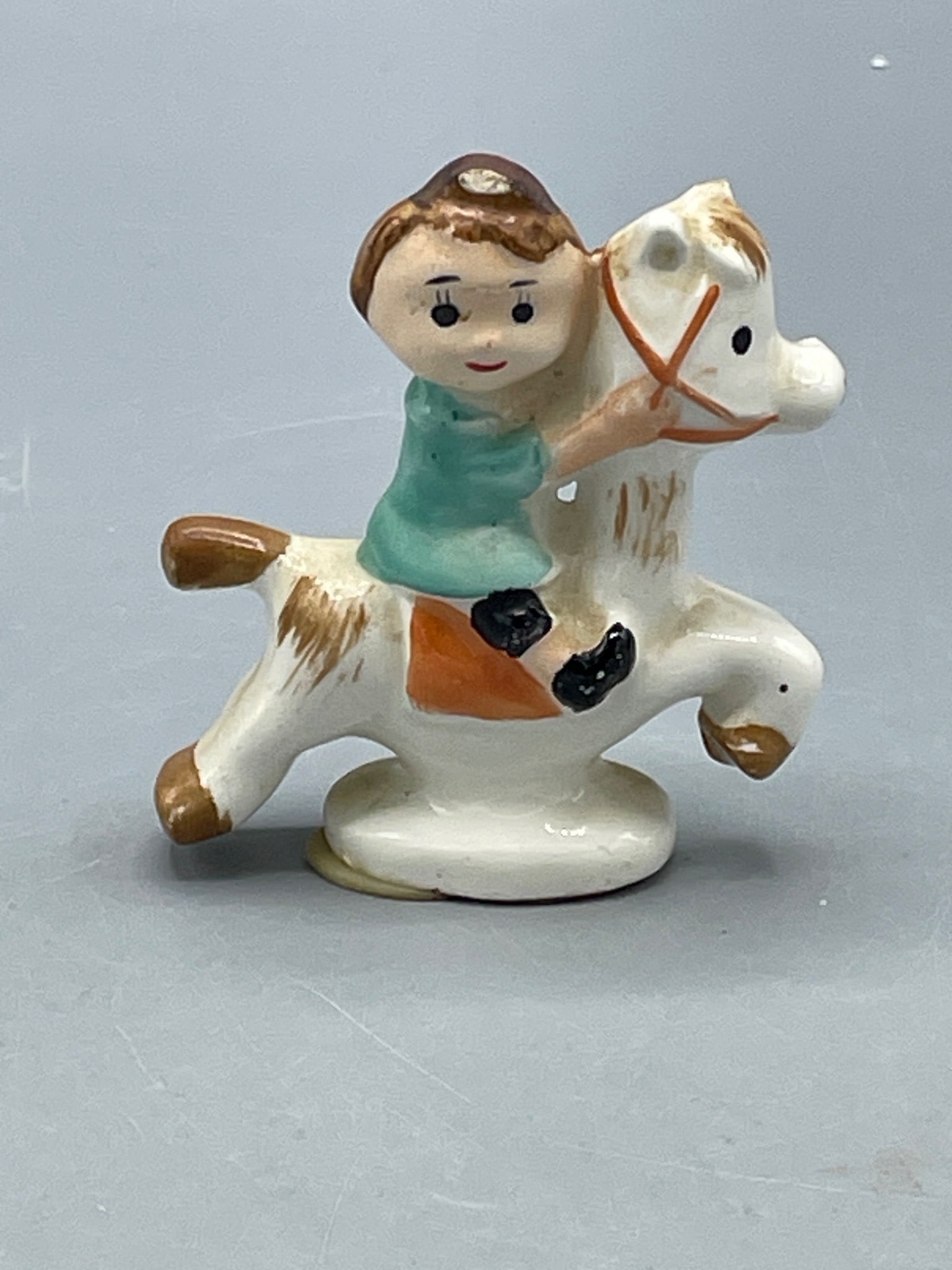 Hand-Painted Ceramic Figurine of Rider on Horseback: This is a hand-painted ceramic figurine depicting a rider on horseback. The figurine features a childlike rider in a green shirt on a detailed white horse with brown accents. Made in USA as indicated