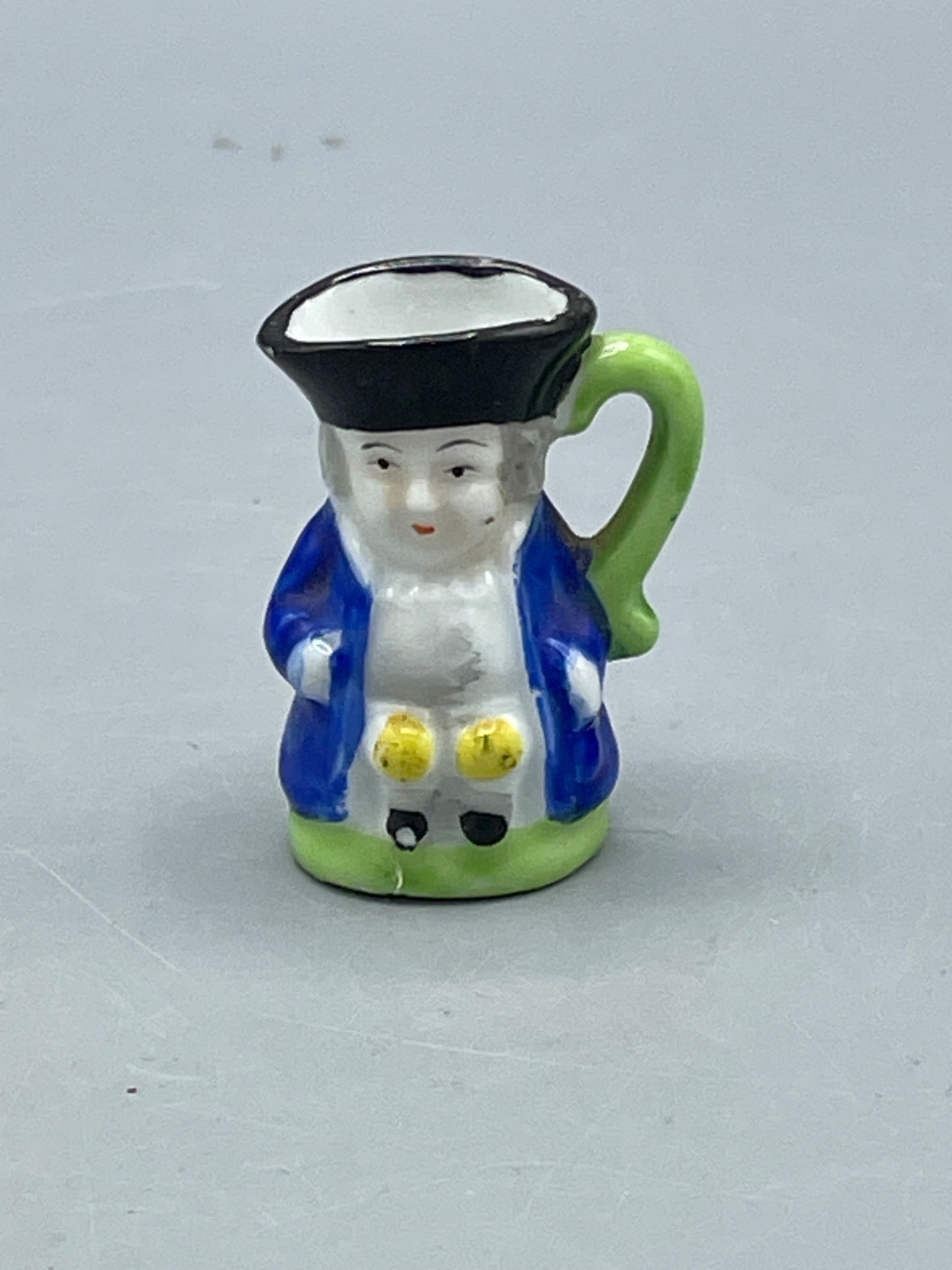 Miniature Ceramic Toby Jug with Japan Marking, 20th Century: A small ceramic Toby jug measuring approximately 2 inches in height, featuring a figural design with painted details in blue, green, black, yellow, and white. The bottom is marked 'JAPAN,' indicating