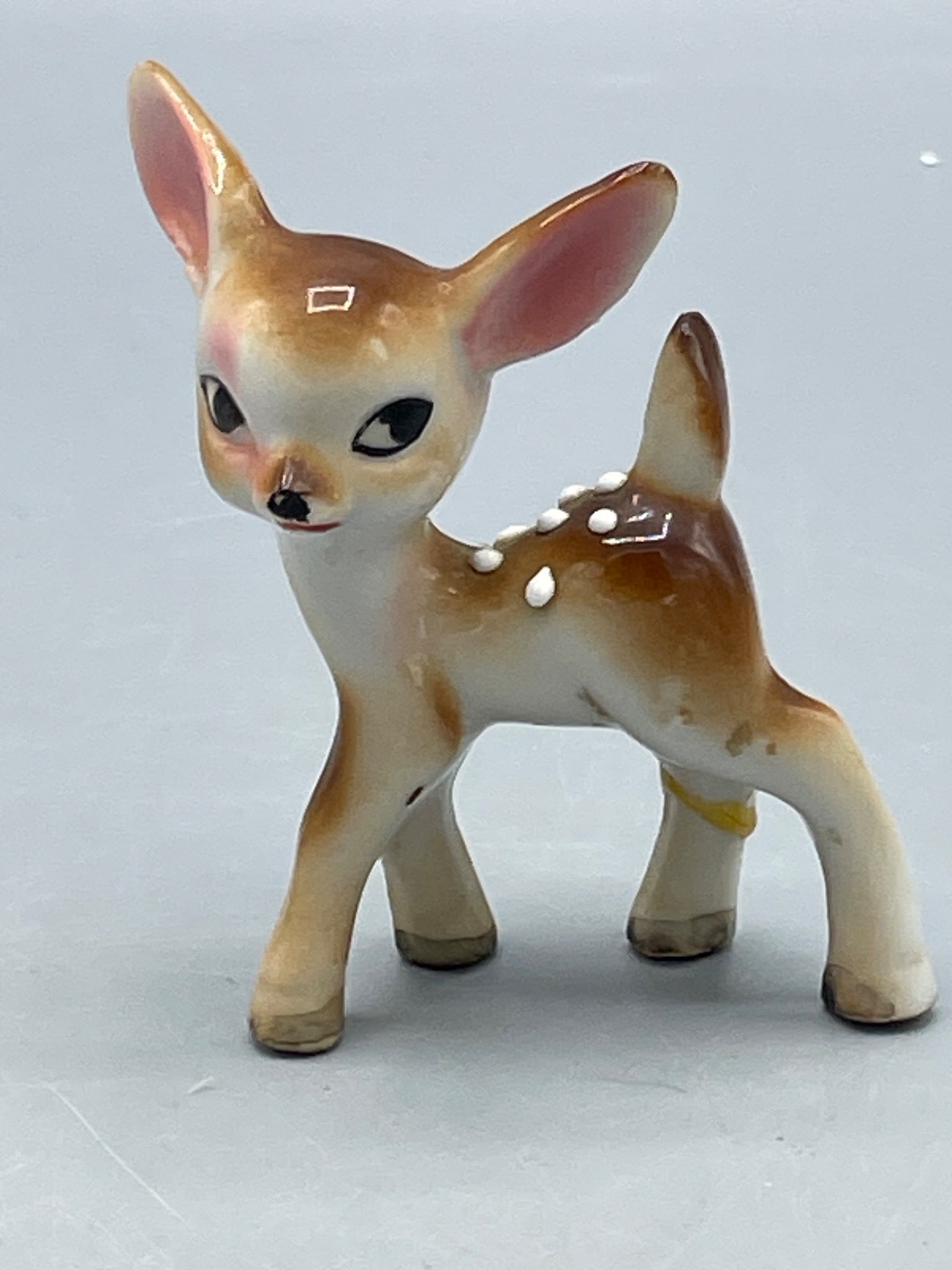 Small Ceramic Deer Figurine with Hand-Painted Details: This is a small ceramic deer figurine standing approximately 3 inches tall. The piece is hand-painted with brown and white tones, including white spotted accents on its back. The underside shows minor