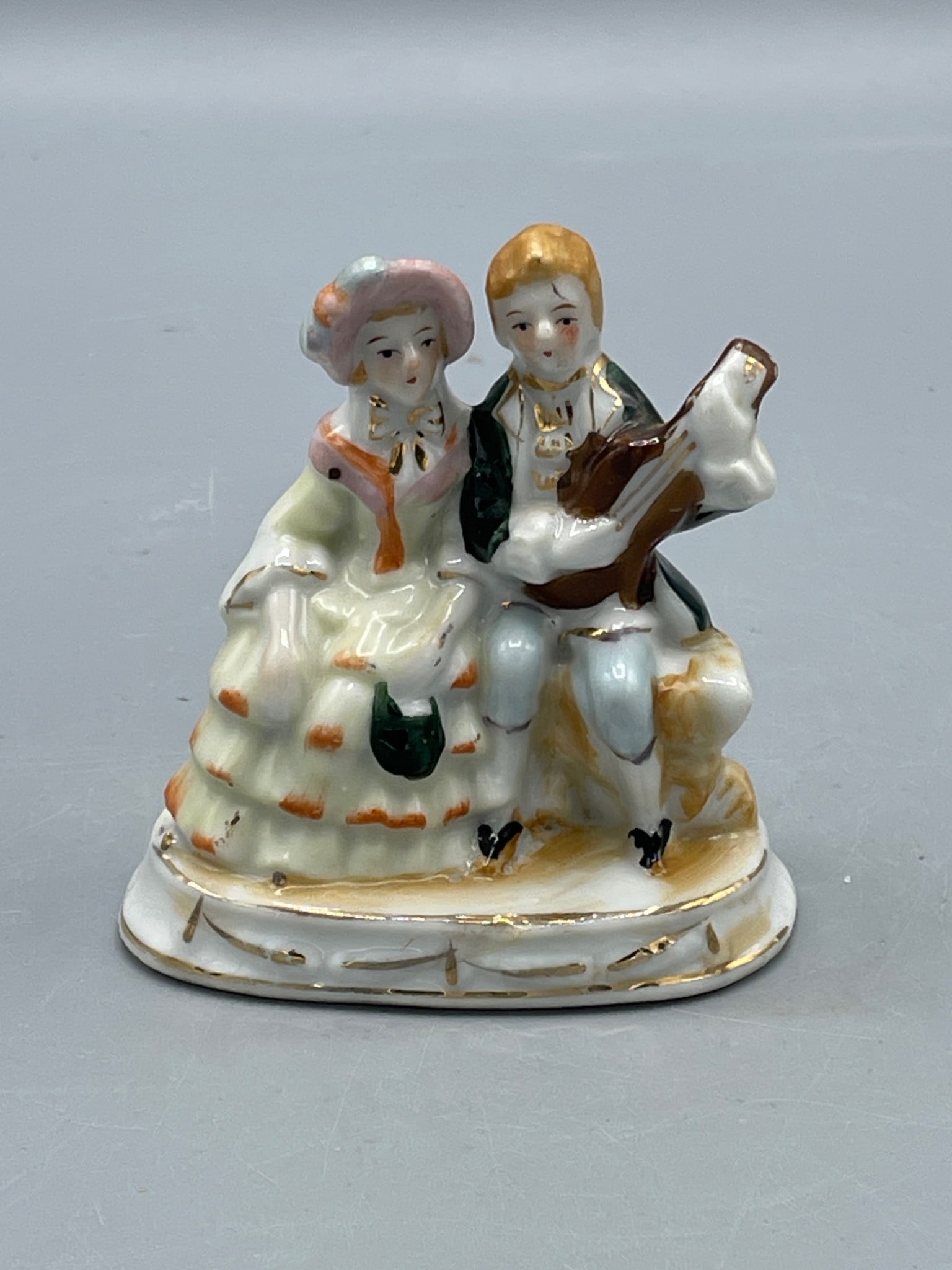 Porcelain Figurine With 'Made in Occupied Japan' Marking: An intricate porcelain figurine depicting a seated couple, with the male character playing a string instrument. Marked 'Made in Occupied Japan' on the underside, indicating production between 1945