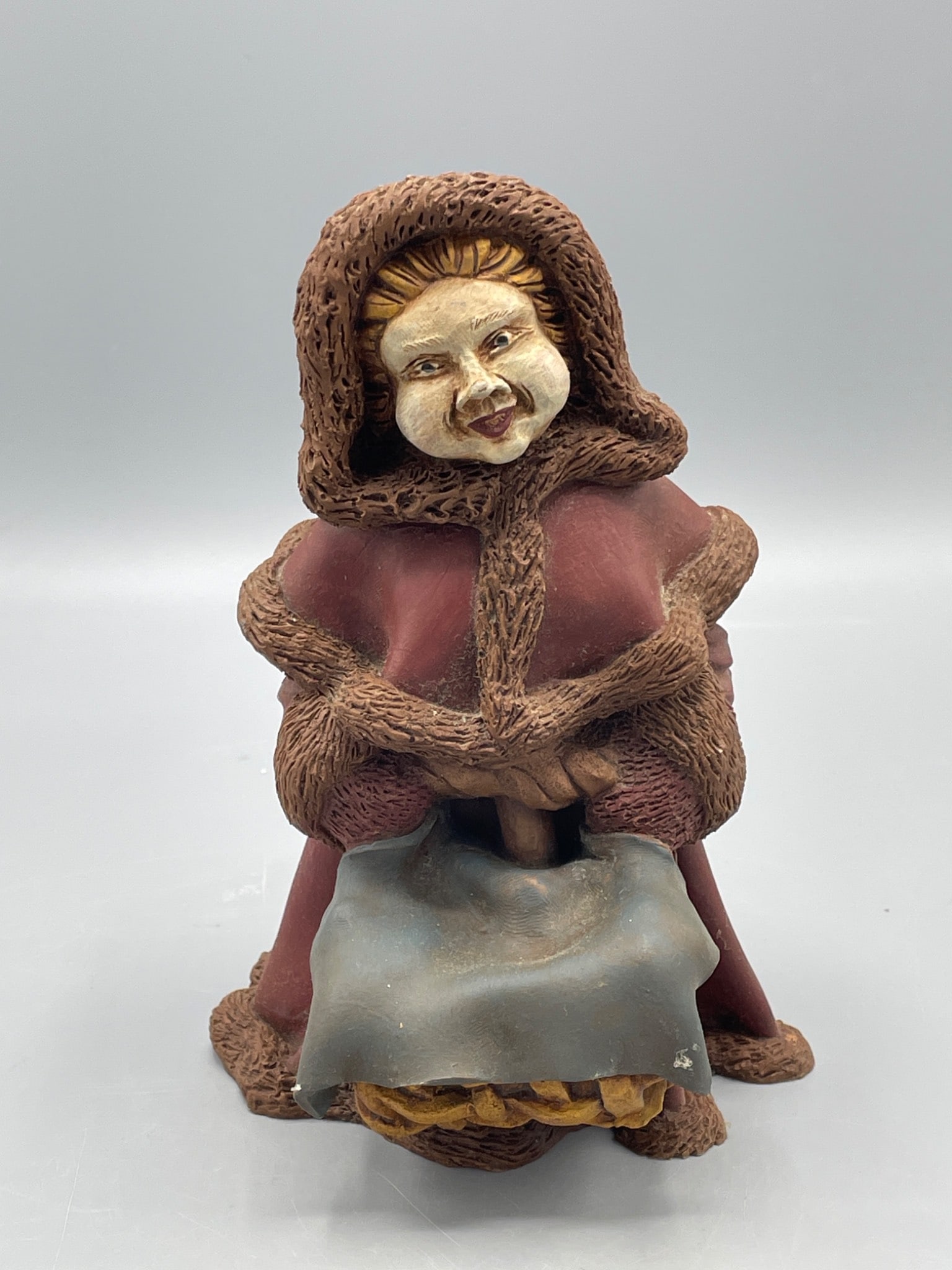 Handcrafted Clay Figurine Depicting Hooded Woman with Basket: A hand-molded clay figurine representing a hooded woman holding a basket. The figurine is painted in muted tones with textured details on the hood and robe. It measures approximately 10 inches in