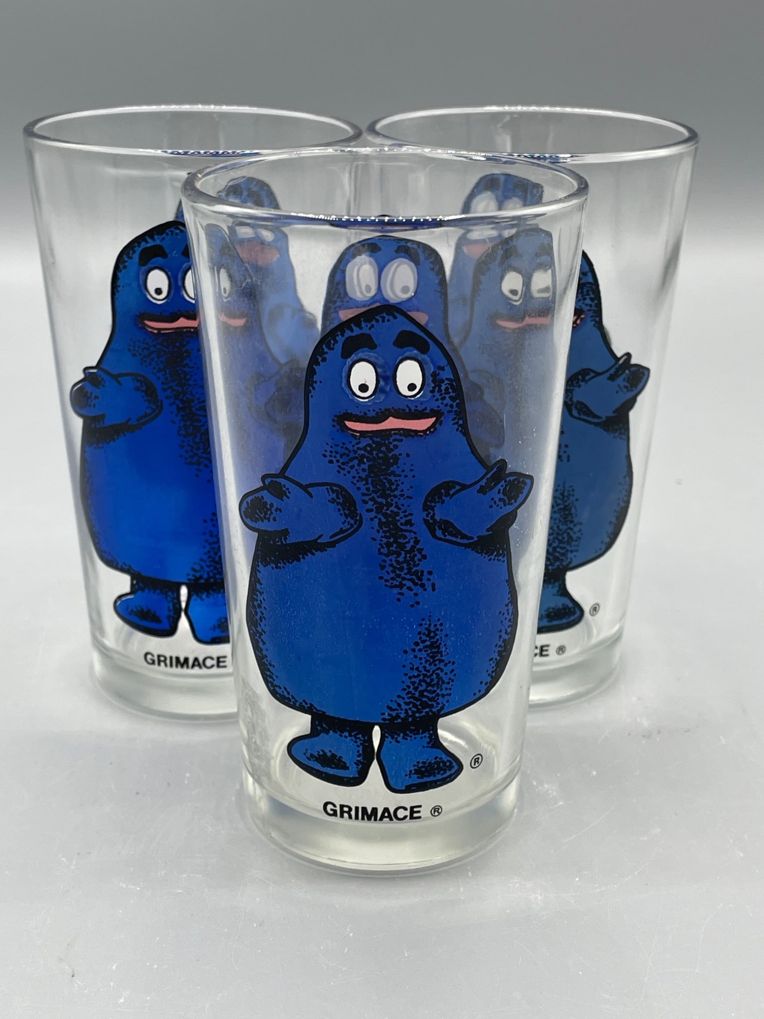 3 McDonald's Grimace Drinking Glasses Featuring Classic Design: This lot includes a set of 3 McDonald's promotional Grimace drinking glasses, featuring a full-color design of Grimace on clear glass. Glasses measure approximately 5 inches in height and 2.75 inches