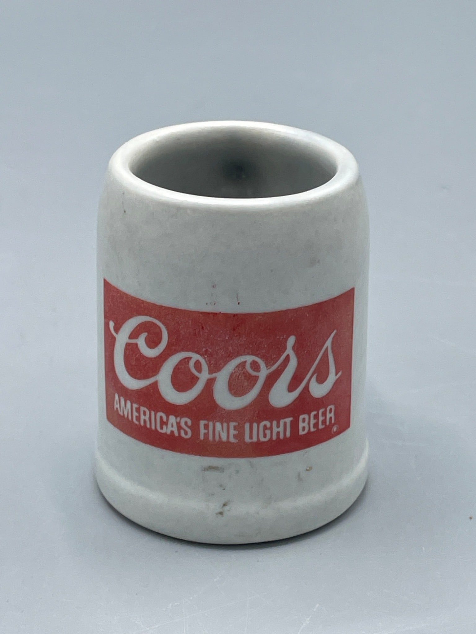 Coors America's Fine Light Beer Ceramic Shot Glass/Mini Mug: This is a ceramic shot glass or mini mug featuring Coors branding with the text 'America's Fine Light Beer' in red and white. The mug has a handle and is approximately 2.5 inches tall. It shows signs