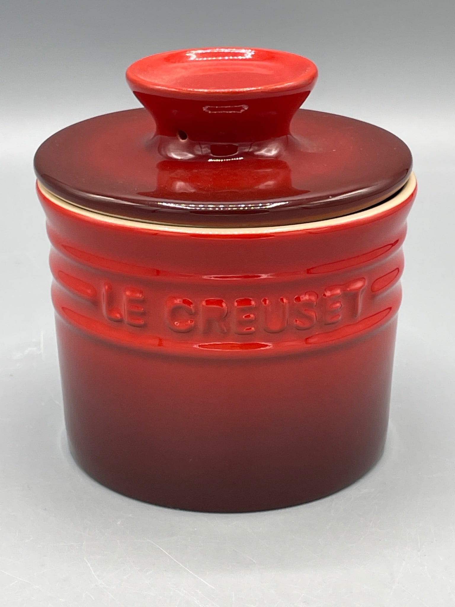 Le Creuset Stoneware Butter Crock in Cerise Red: Le Creuset stoneware butter crock in cerise red. The crock is ideal for storing softened butter at room temperature. Features include a ceramic body with embossed branding, a lid that doubles as a