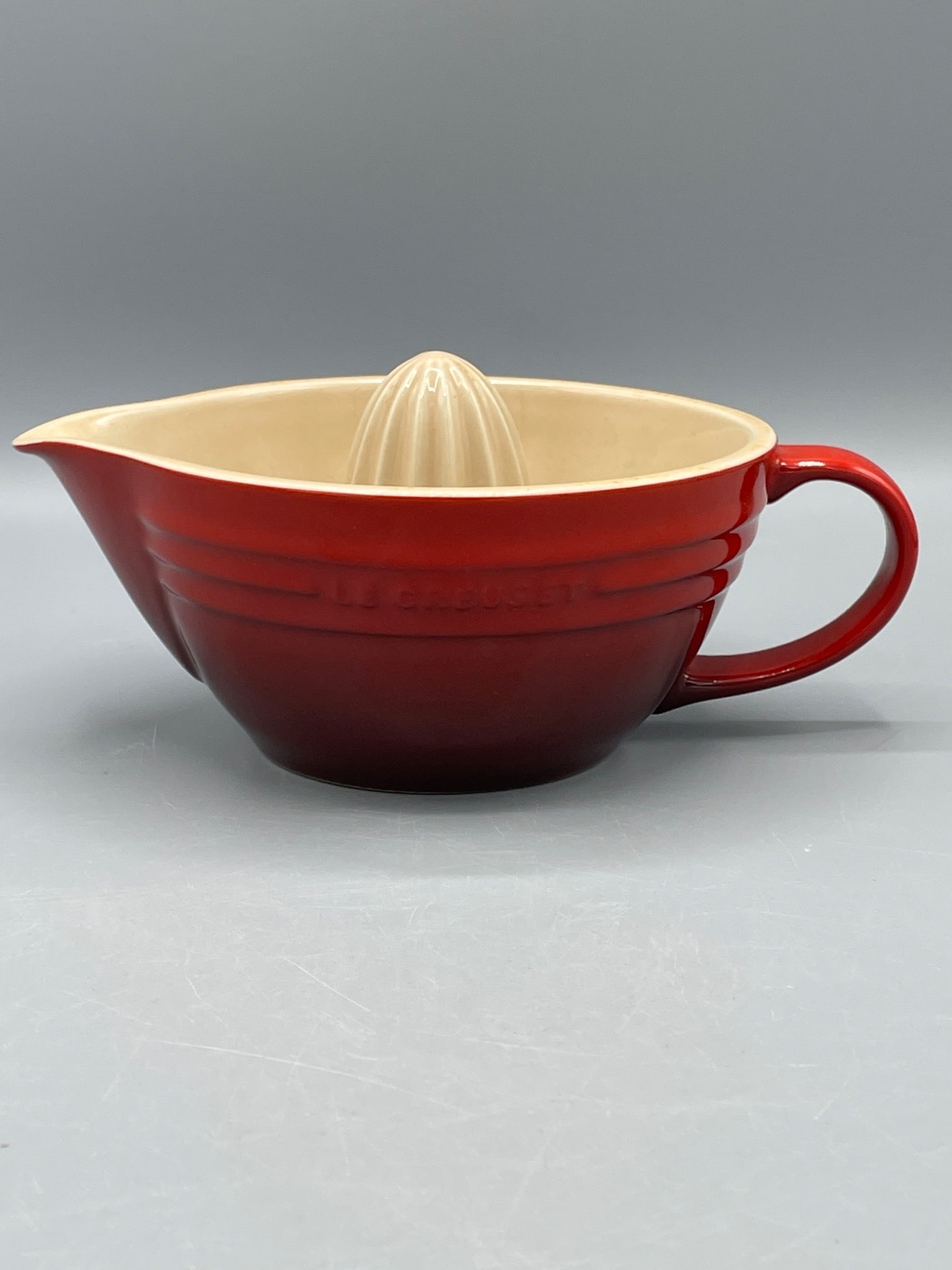 Le Creuset Red Ceramic Juicer With Handle and Pour Spout: This Le Creuset ceramic juicer features a bright red exterior with a beige interior. It includes an integrated juicing cone for extracting citrus juice, a functional handle, and a pour spout for ease
