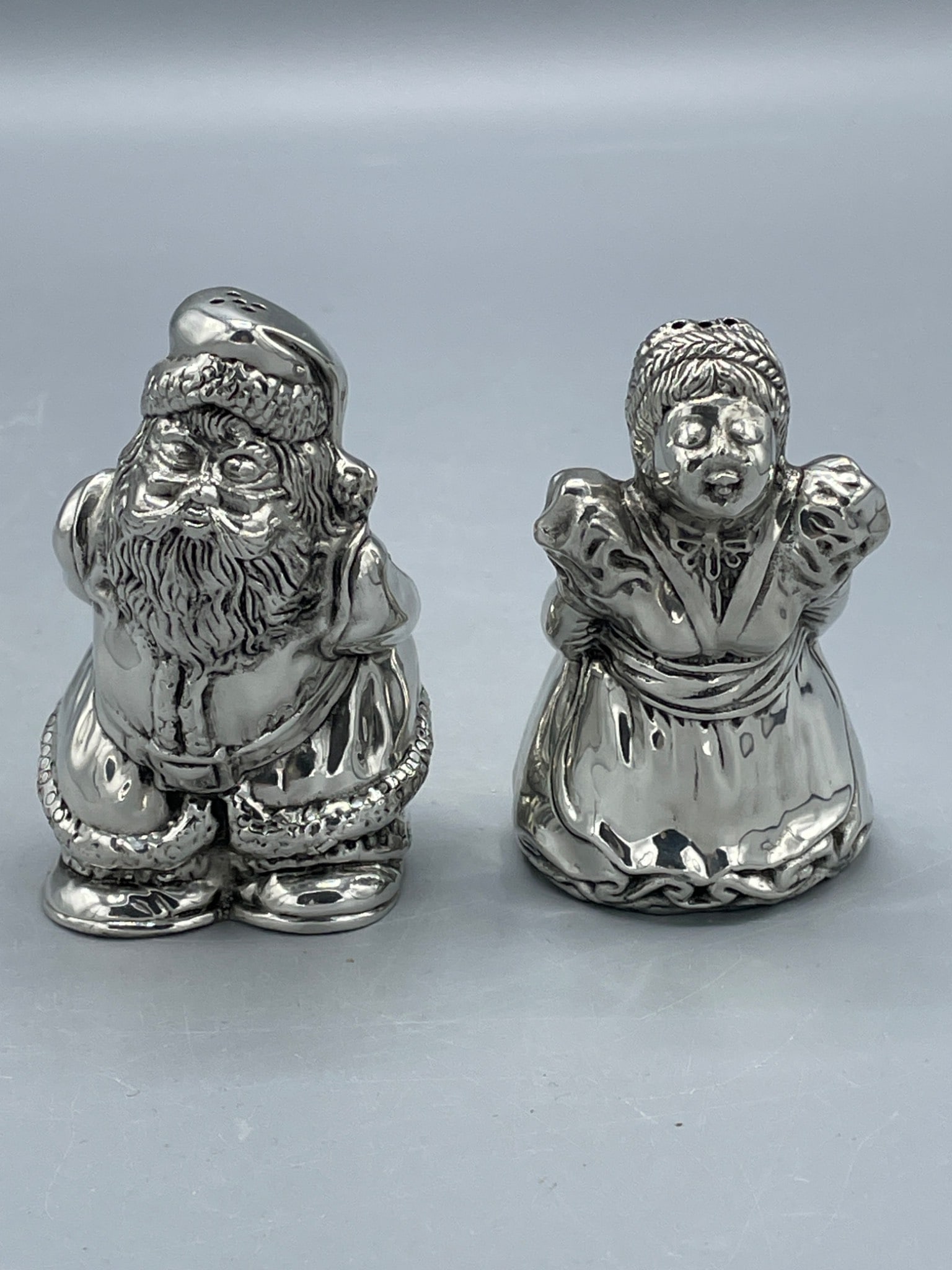 Kirk Stieff Pewter Santa and Caroler Salt and Pepper Shakers, Made in Thailand: Kirk Stieff pewter salt and pepper shakers in the shape of a Santa Claus and a caroler figure. Markings on the base indicate 'Kirk Stieff Pewter 716' and 'Made in Thailand.' Each shaker has a rubber s