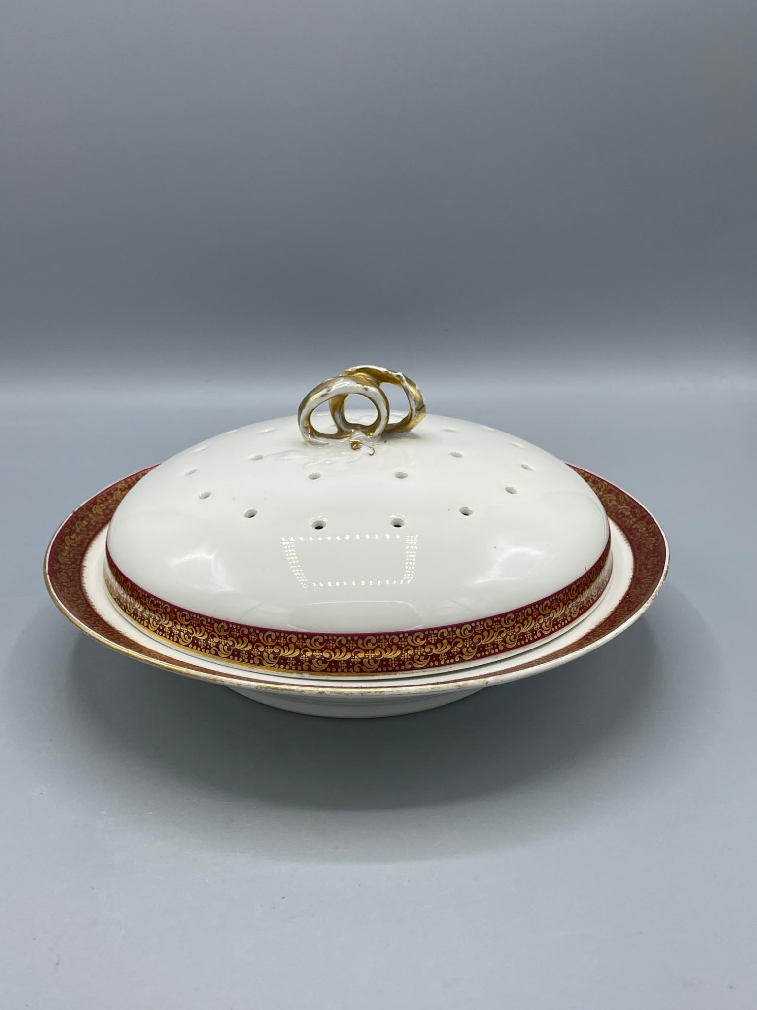 GDA Limoges Porcelain Covered Dish With Perforated Lid and Gold Trim: This listing features a GDA Limoges porcelain covered dish with a perforated lid. The lid features a gold-painted handle, and the dish is adorned with a red and gold trim pattern. The bottom is