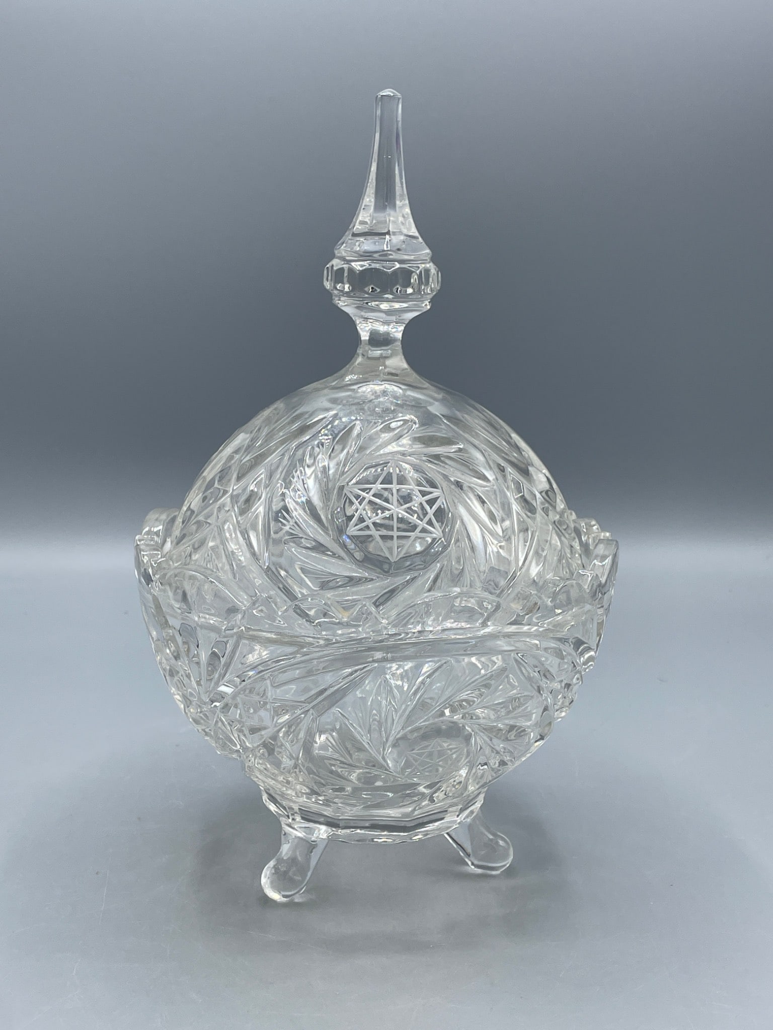 Clear Cut Glass Pedestal Candy Dish With Lid And Star Etching: Clear cut glass pedestal candy dish with a removable lid, featuring a star design etched on both the base and lid. The dish includes three raised legs and a finial handle on the lid. The piece measure