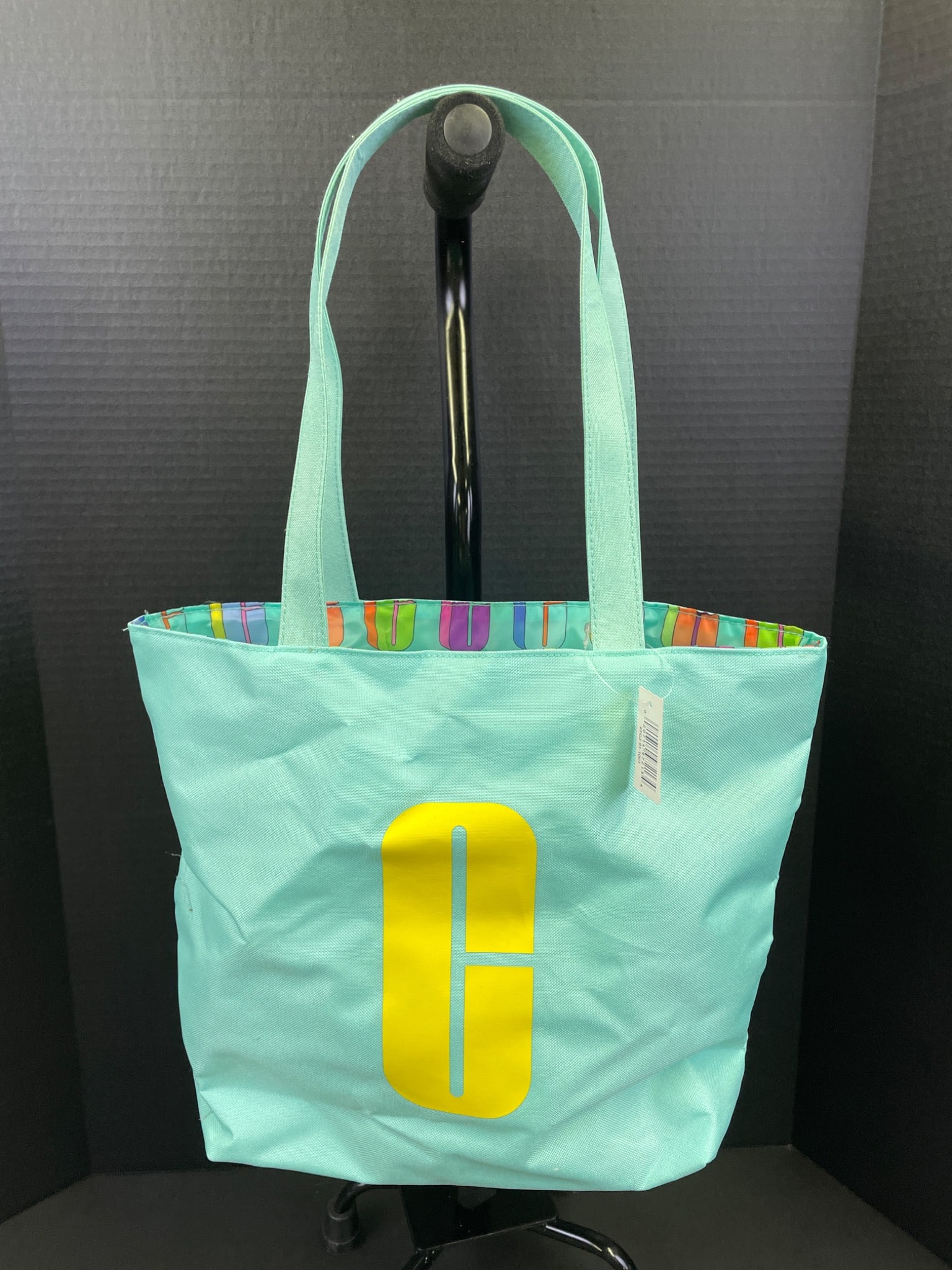 Clinique Light Blue Tote Bag with Multicolored Interior Pattern: Clinique lightweight tote bag featuring a light blue exterior with a large yellow 'C' logo on the front. The interior has a multicolored graphic design. Includes two shoulder straps and original