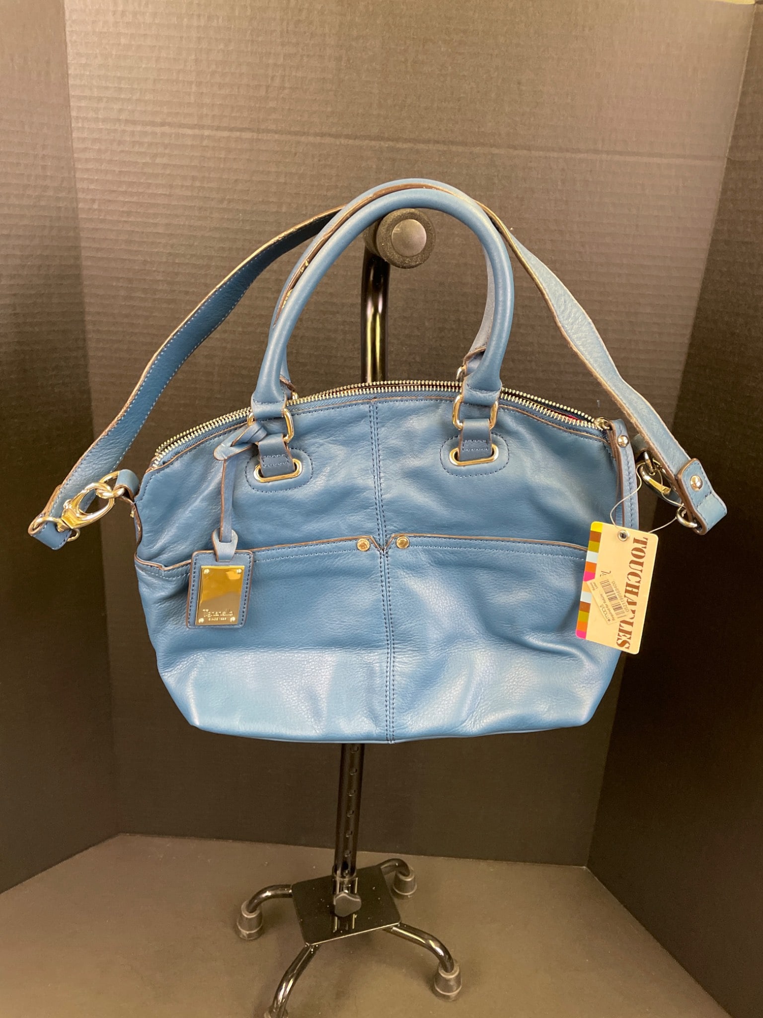 Blue Leather-Handbag With Adjustable Strap And Multicolored Interior: This handbag is constructed from blue leather and includes dual carrying handles and an adjustable strap. The interior is lined with a colorful striped fabric and features multiple pockets for