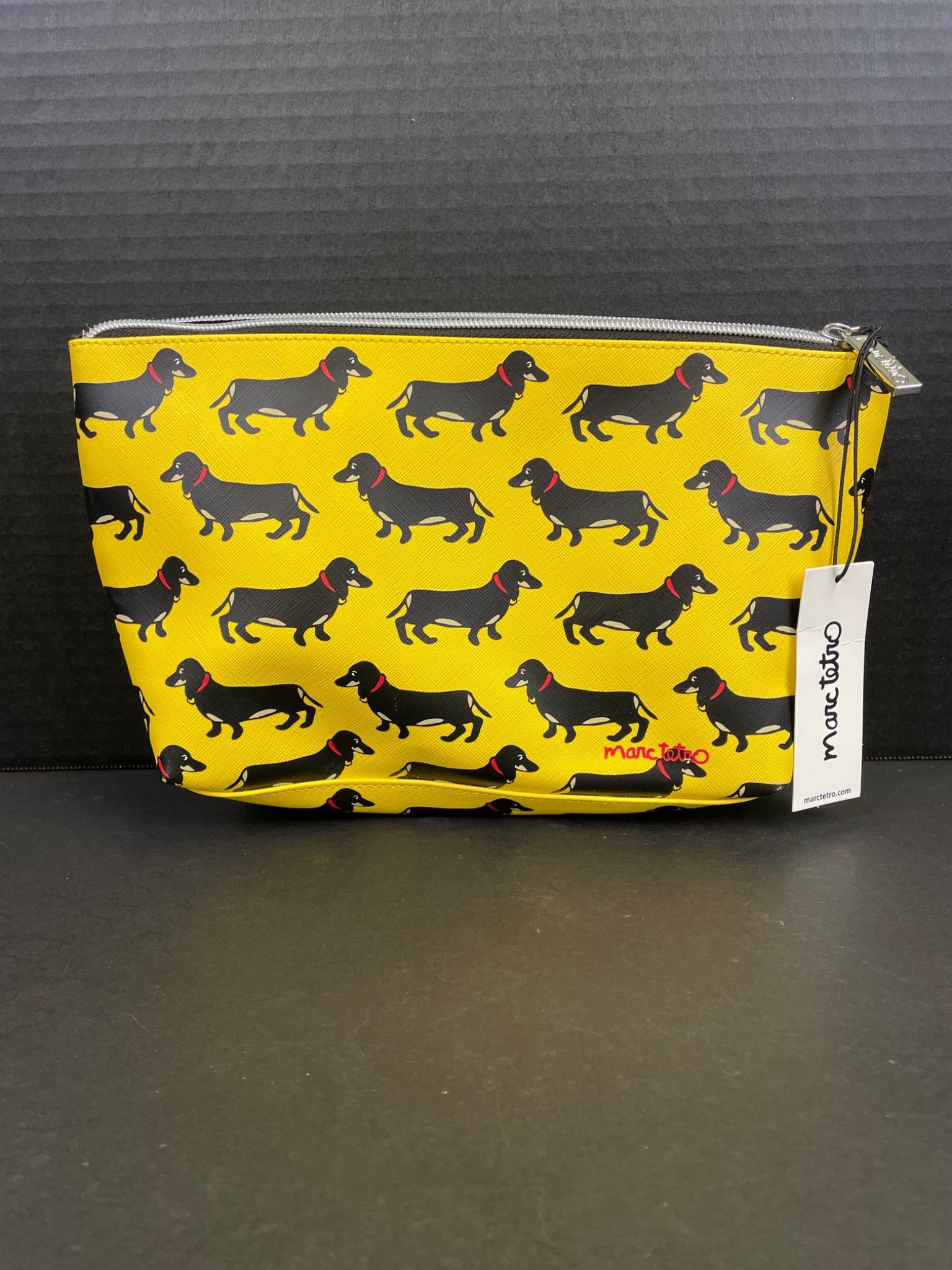 Marc Tetro Yellow Zip Pouch With Dachshund Print: Marc Tetro zip pouch with a yellow exterior featuring an allover dachshund print. Includes a black and white striped interior lining. The pouch has a silver zipper closure and a branded Marc Tetro