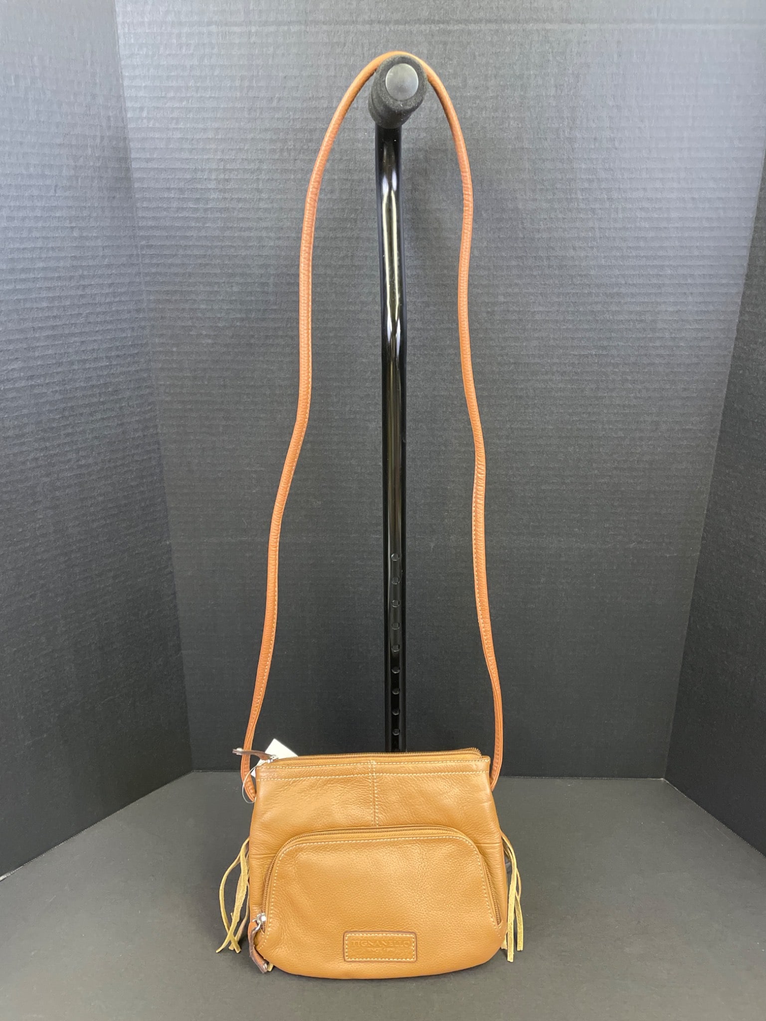Tignanello Crossbody Bag With Fringe Trim and Adjustable Strap: Tignanello crossbody bag featuring a front zip pocket, fringe trim, and adjustable strap. The interior includes striped lining, multiple sections, and a zippered pocket. Brand tag attached. Made of