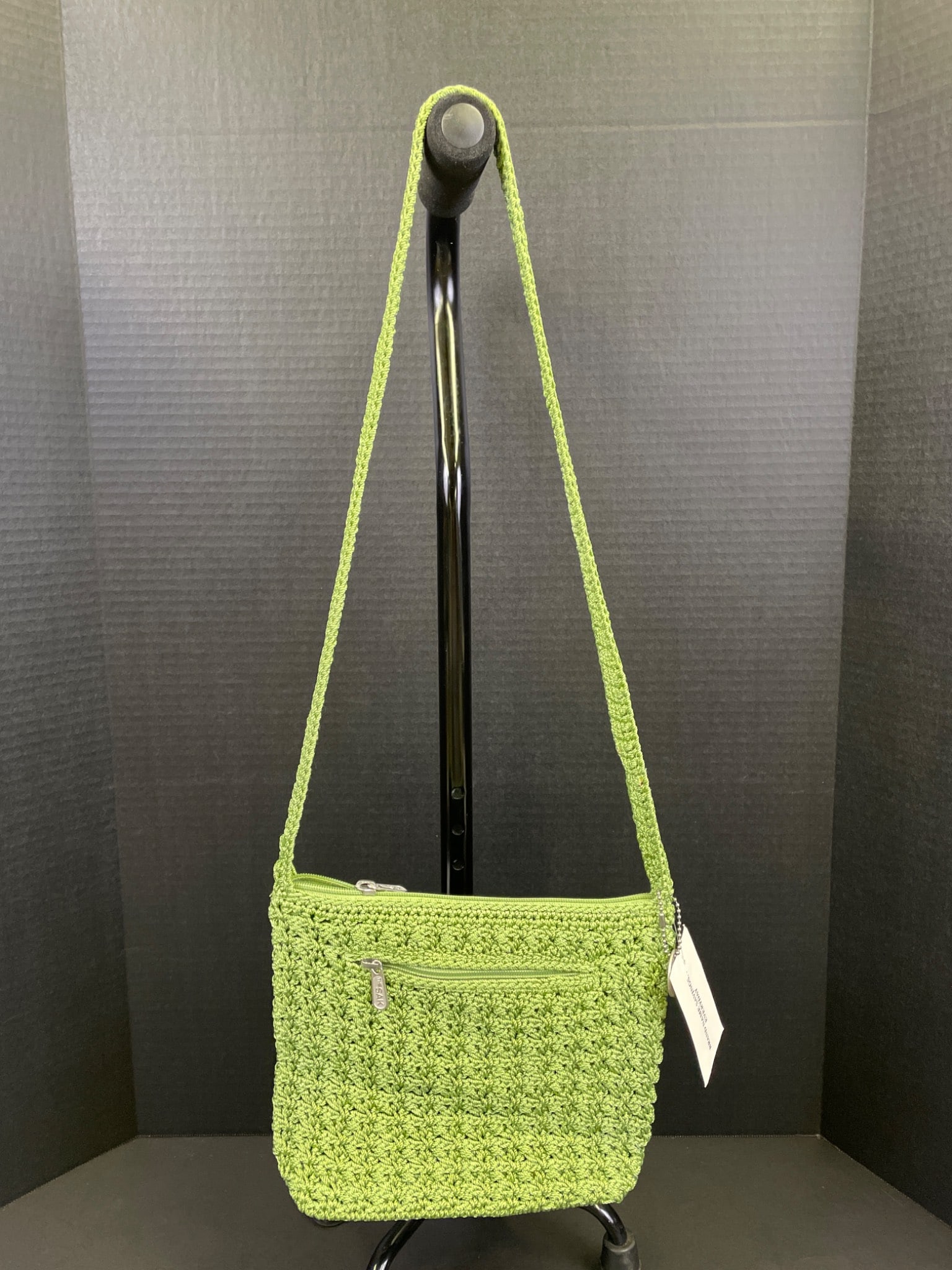 The Sak Original Handmade Crochet Shoulder Bag in Green: The Sak Original crochet handmade shoulder bag in green with zipper closure. Features an adjustable crochet strap and a lined interior with compartments. Includes original tags, indicating it is