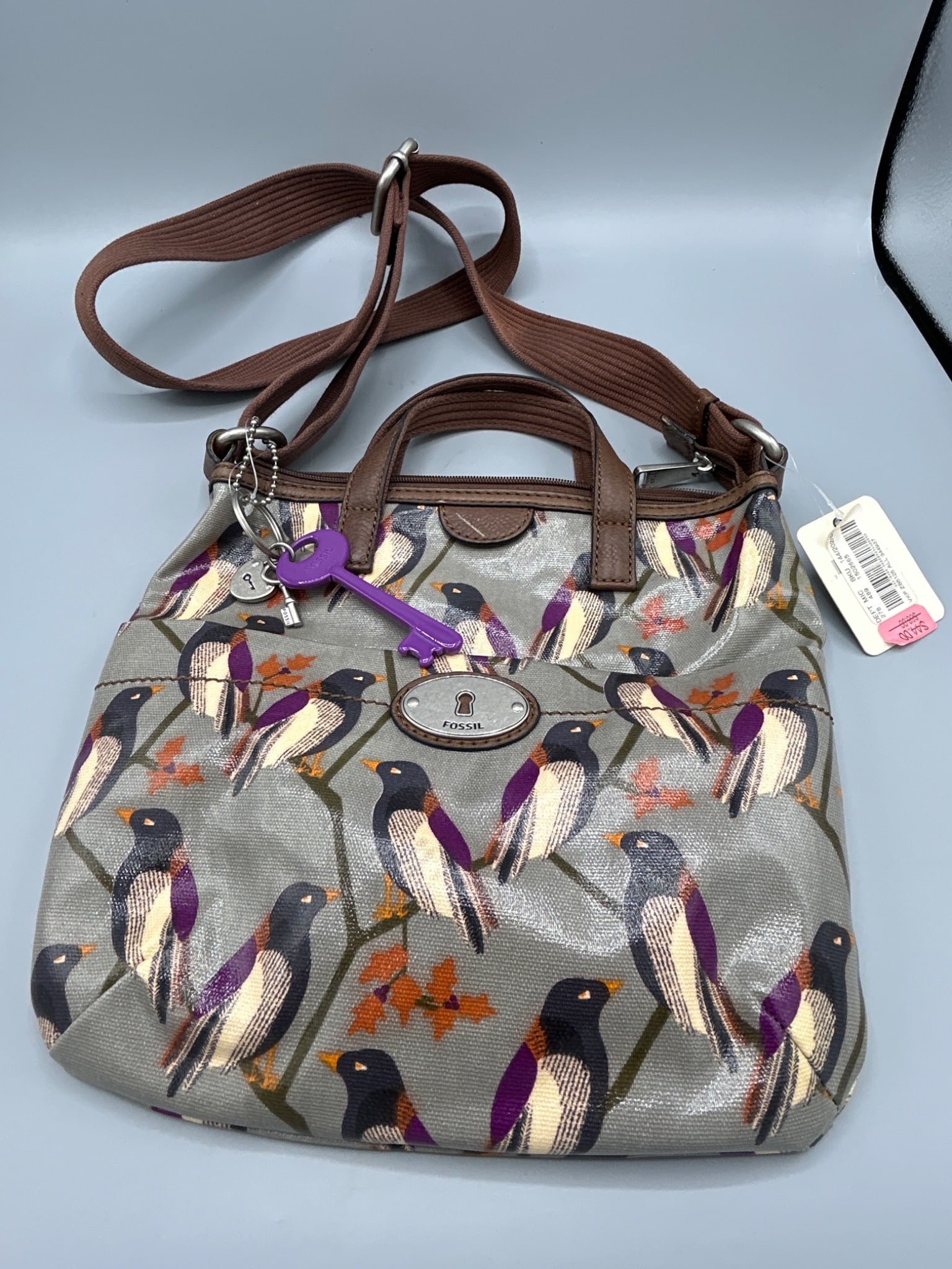 Fossil Key-Per Crossbody Bag with Multicolor Bird Print: Fossil Key-Per crossbody bag featuring a multicolor bird print. The bag includes dual handles, an adjustable crossbody strap, and secure zipper closure. The interior is fabric-lined with a purple and