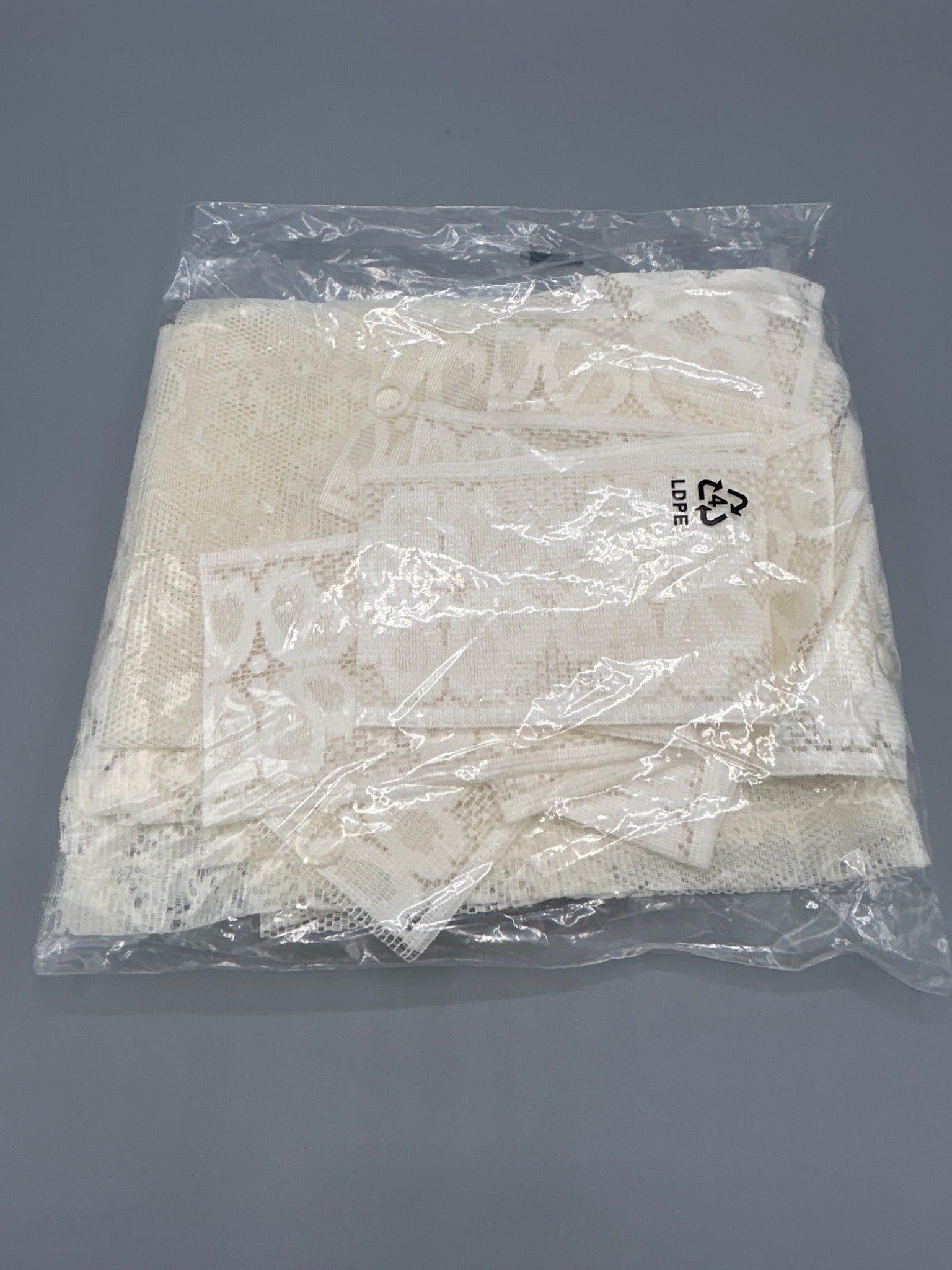 White Lace Fabric Pack in Transparent Packaging: A pack of white lace fabric, enclosed in transparent LDPE packaging. The material features detailed lace patterns, suitable for various applications. Dimensions, weight, and year of manufacture are un