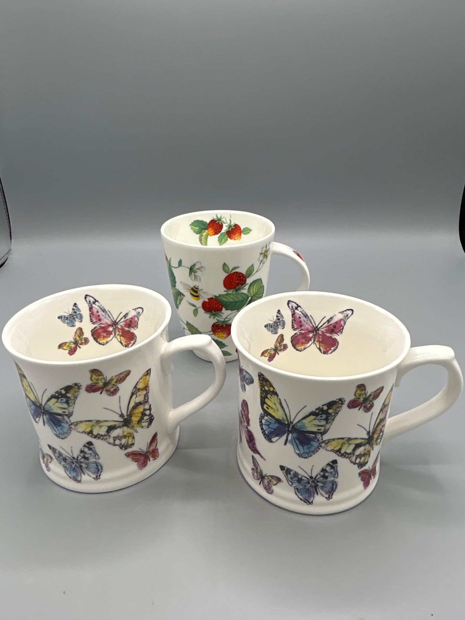 3 Fine China Mugs by Roy Kirkham and Cooksmart (2000 and Model 787202/787188): This lot consists of three fine china mugs, including two by Cooksmart featuring butterfly designs (model numbers 787202 and 787188) and one by Roy Kirkham in the 'Alpine Strawberry' pattern, dated