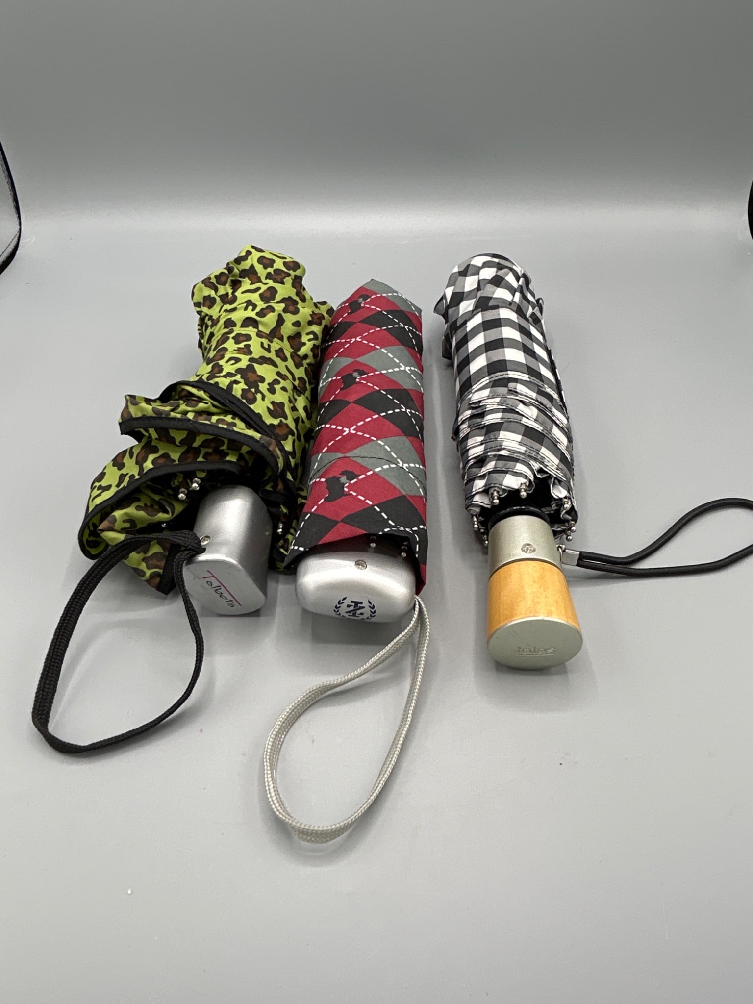 3 Folding Umbrellas by Talbots, Totes, and an Unbranded Manufacturer: This lot includes three compact folding umbrellas, each featuring a unique handle. Brands represented are Talbots, Totes, and a third unidentified manufacturer symbolized with a crest logo. Each umbre