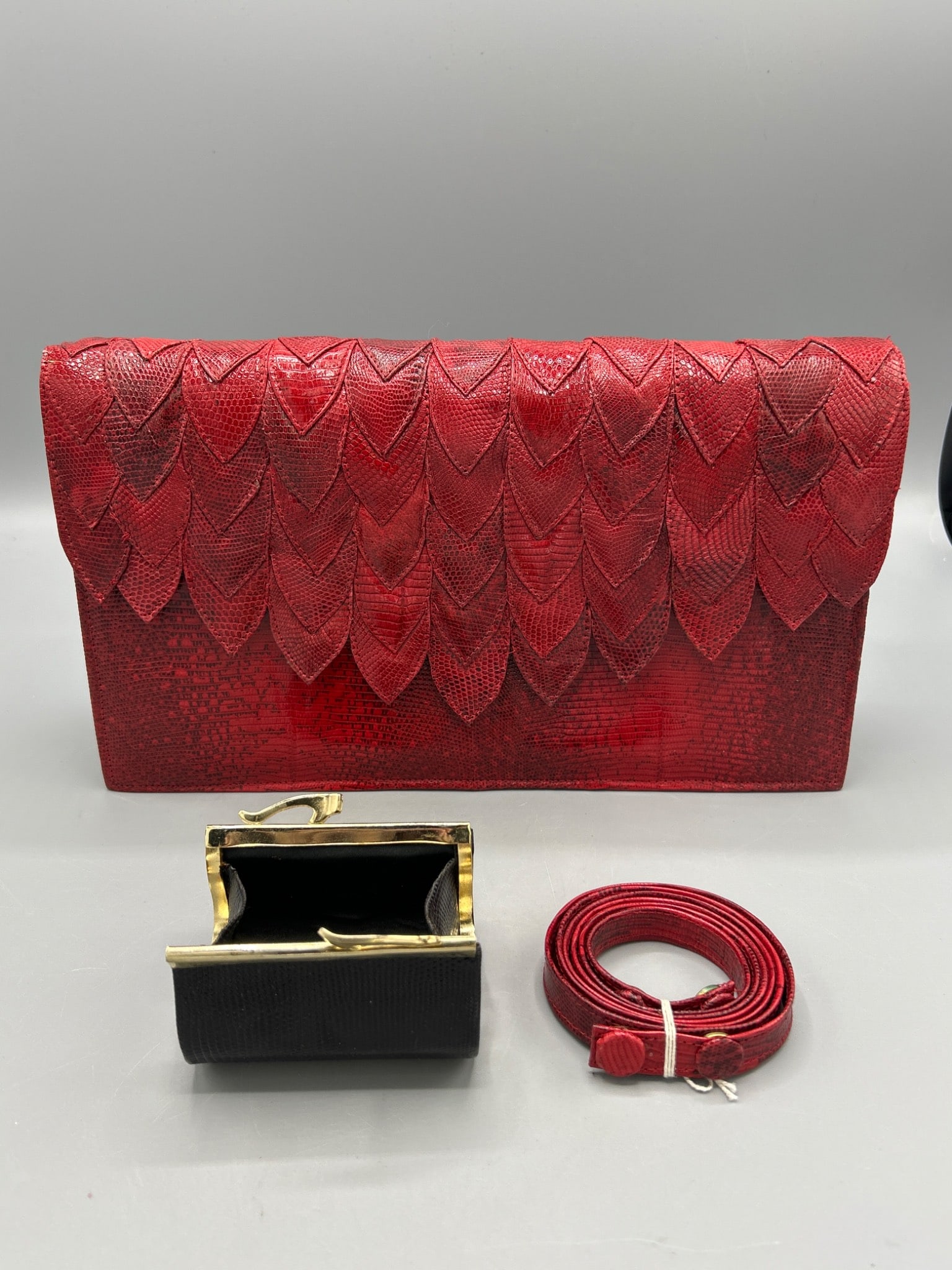 R. SaldaÃ±a House of Reptile Red Lizard Skin Clutch Bag With Accessories: This item is a red lizard skin clutch bag designed by R. SaldaÃ±a for House of Reptile, featuring a detailed layered scalloped pattern on the flap. The set includes a detachable strap and a