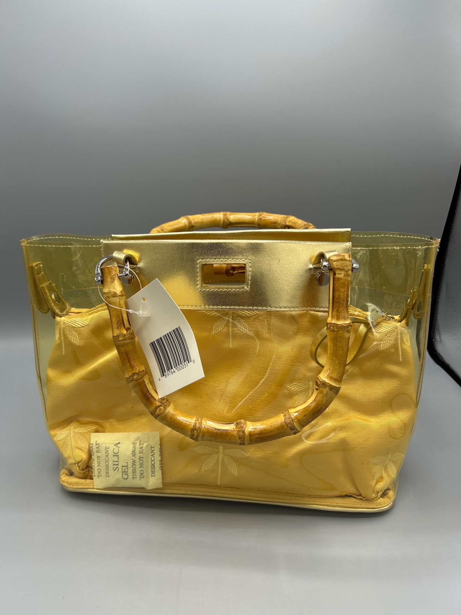 Translucent Gold Handbag With Bamboo Handles: This handbag features a translucent gold outer layer, bamboo handles, and a gold-tone interior pouch with a zip closure. It includes a top magnetic clasp and measures approximately 11.5 inches in