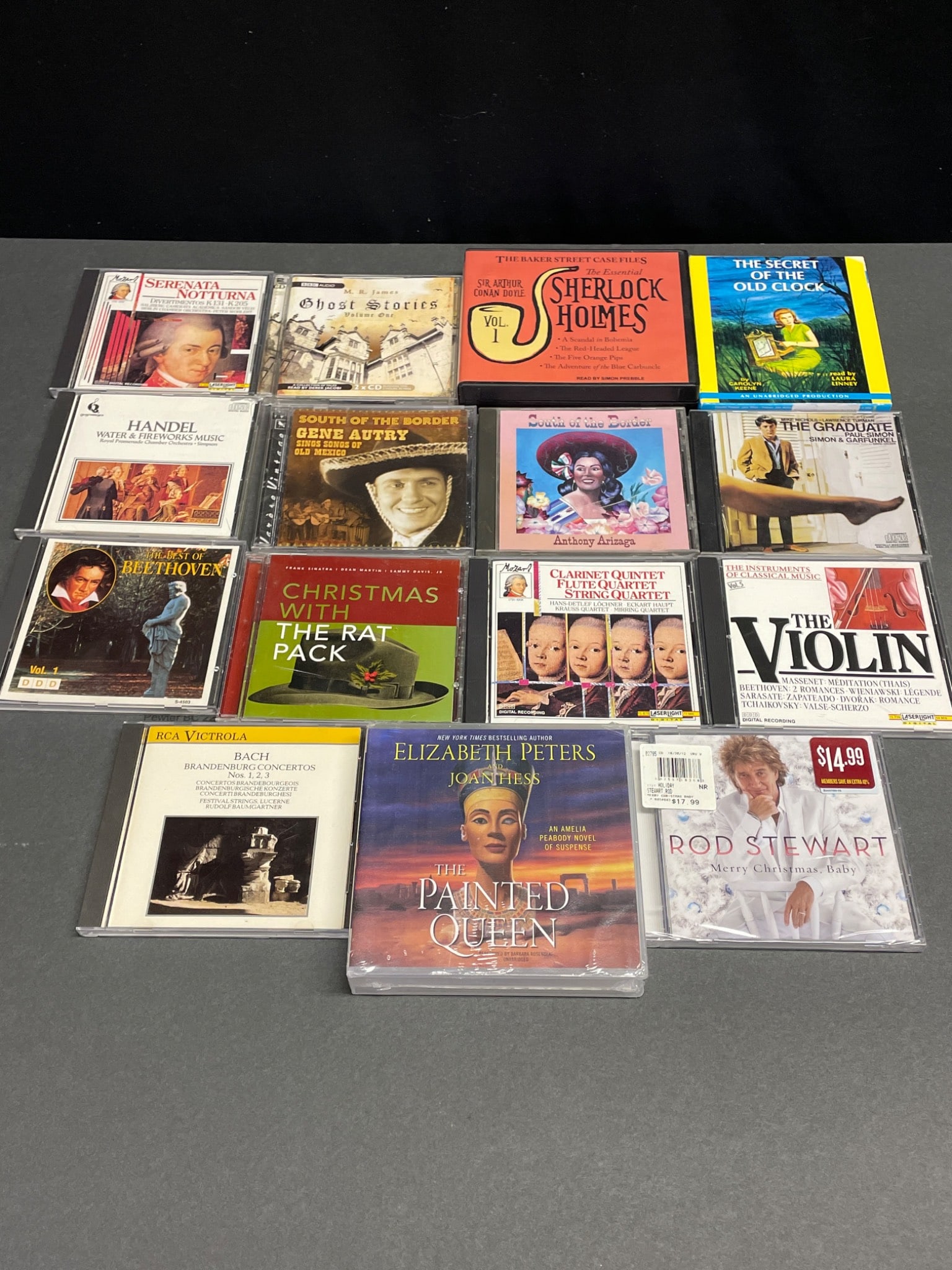 16 Music and Audiobook CDs Featuring Various Artists and Genres: This lot consists of 16 CDs, featuring various genres including classical, holiday music, soundtracks, and audiobooks. Highlights include 'Sherlock Holmes Vol. 1,' 'The Graduate' soundtrack, 'Rod Stew
