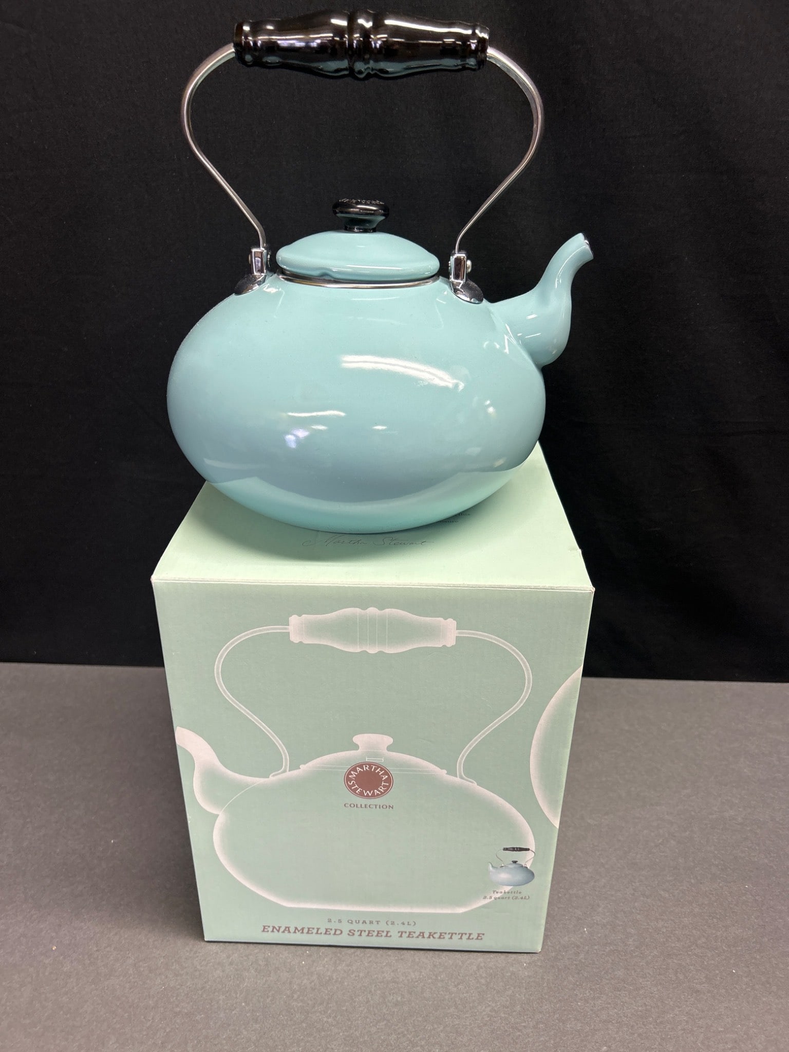 2.5 Quart Enameled Steel Teakettle in Light Blue - Martha Stewart Collection: This is a 2.5 quart (2.4 L) enameled steel teakettle in a light blue finish from the Martha Stewart Collection. The kettle features a black wooden handle with chrome accents, a spout-mounted whistle, 