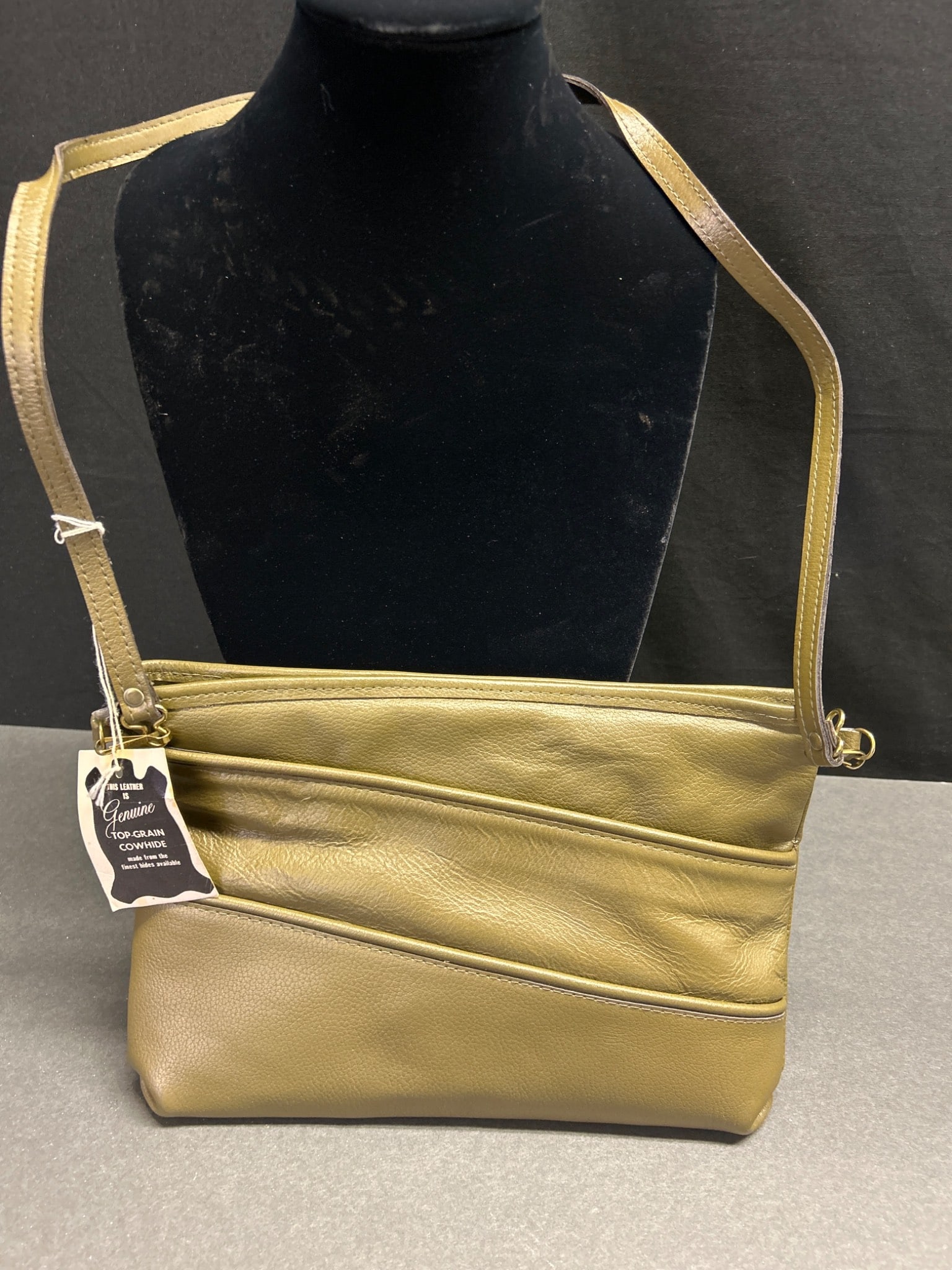 Genuine Top-Grain Cowhide Leather Shoulder Bag with Gold-Tone Finish: This shoulder bag is crafted from genuine top-grain cowhide leather and features a gold-tone finish. The tag affixed to the product indicates that it is made from the finest hides available. The bag